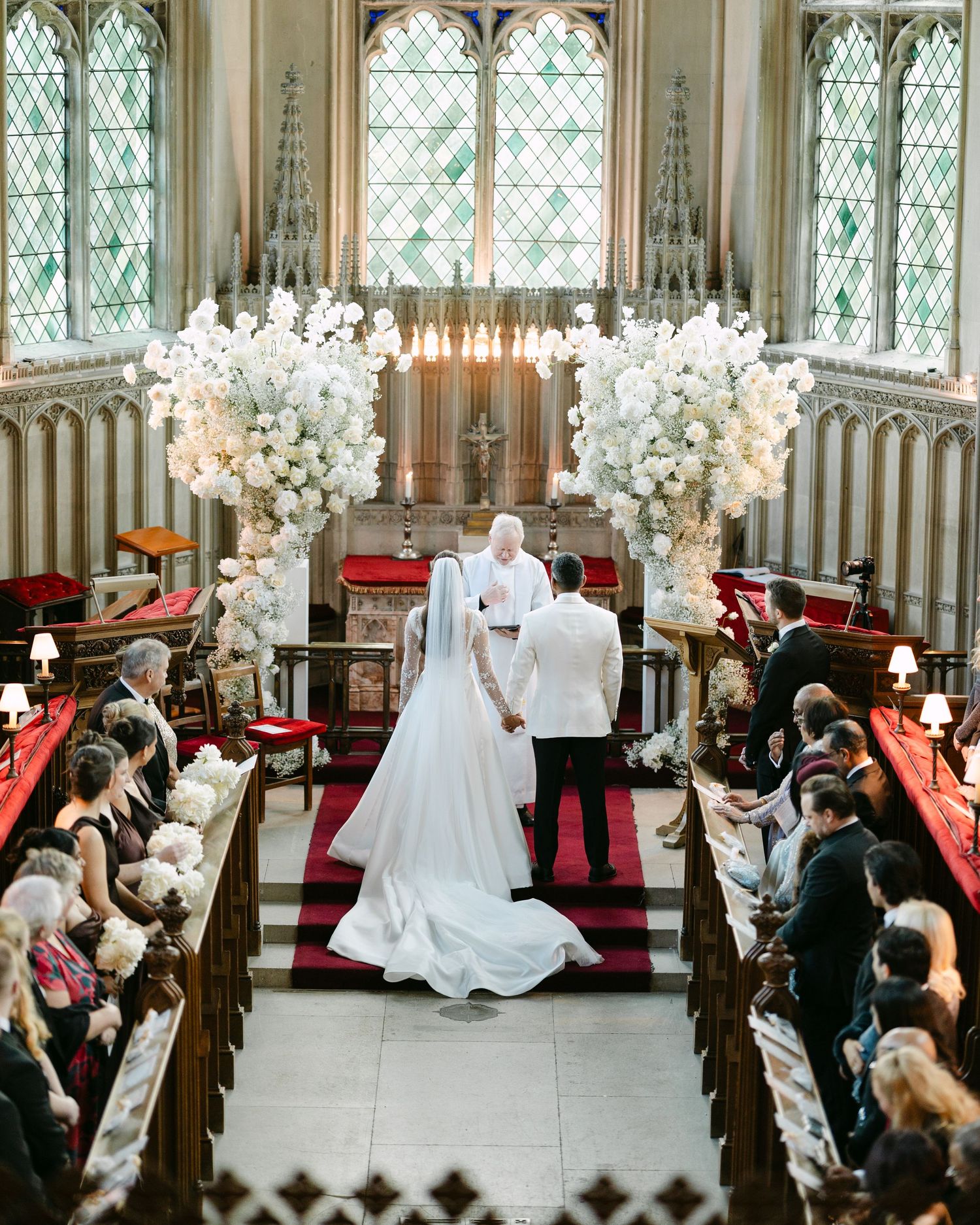 Grand church ceremony with gothic windows, red carpet, and white floral decorations.