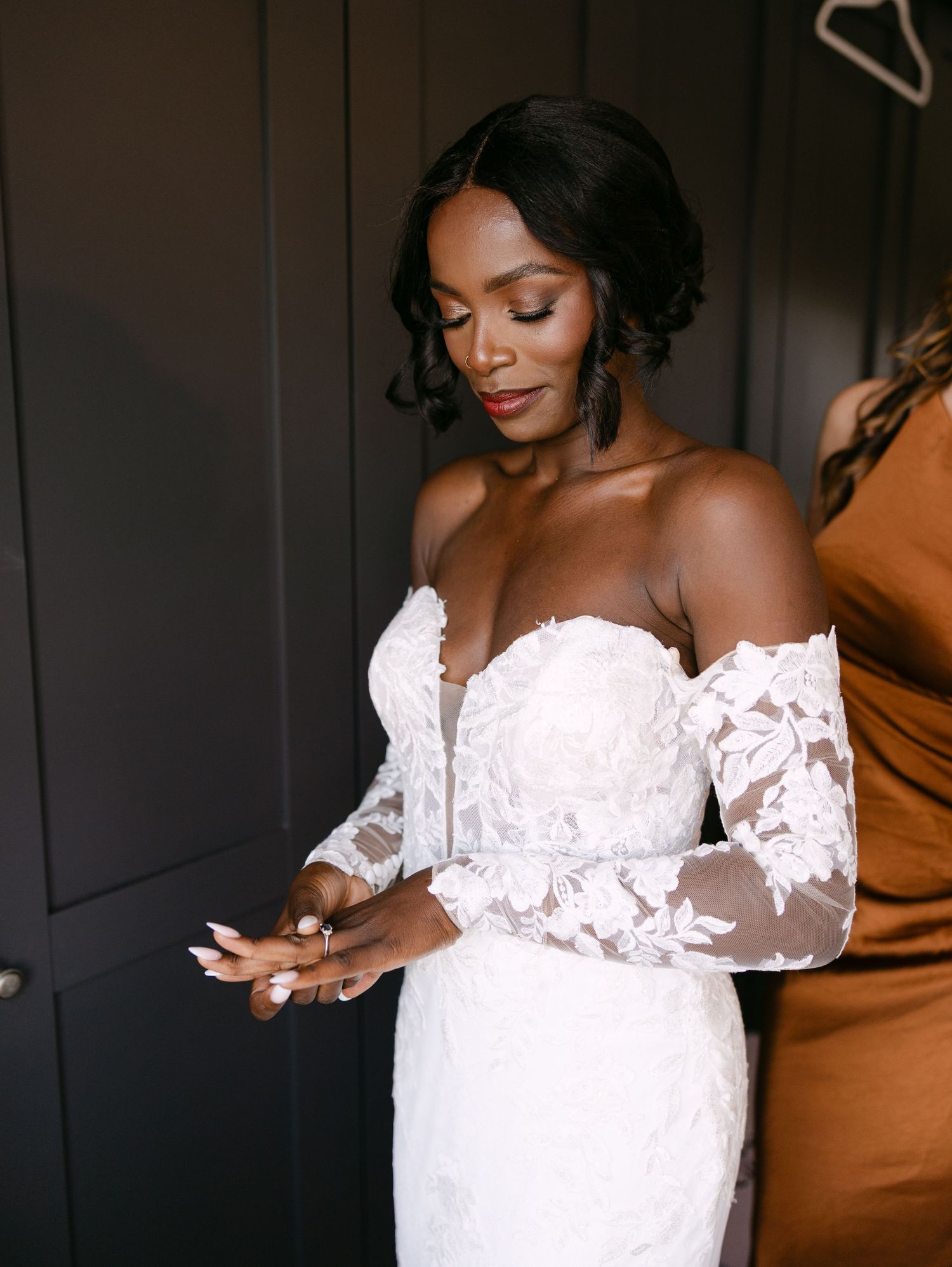 An elegant off-shoulder lace wedding dress being fitted during preparation.