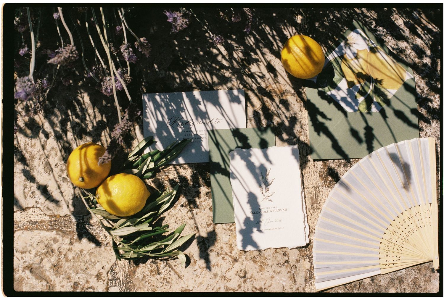Flat lay of lemons, lavender, stationery cards, and a white fan arranged on a sunlit stone surface.