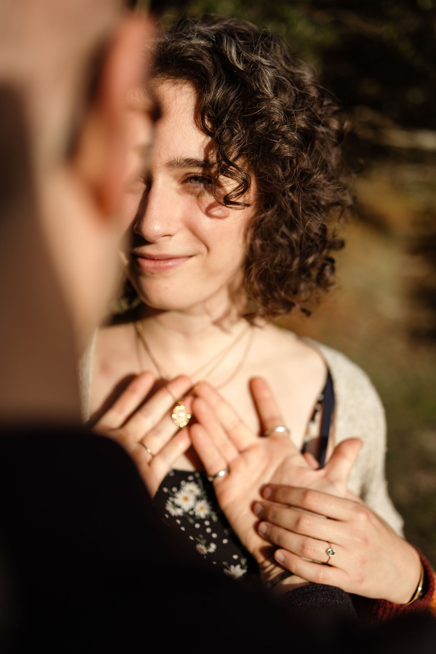 A person wearing a cream sweater shows off their engagement ring with joy.