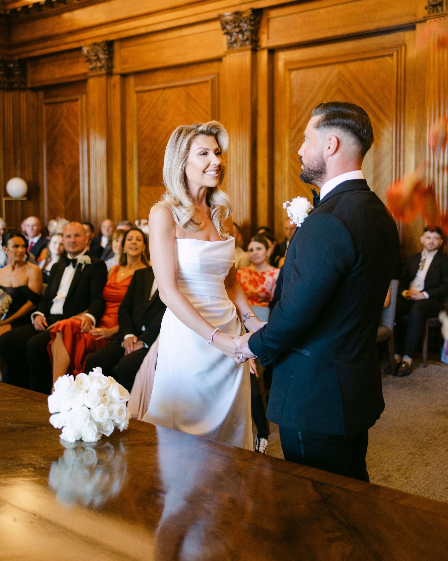 A wedding ceremony in a grand wood-paneled room with ornate architectural details.