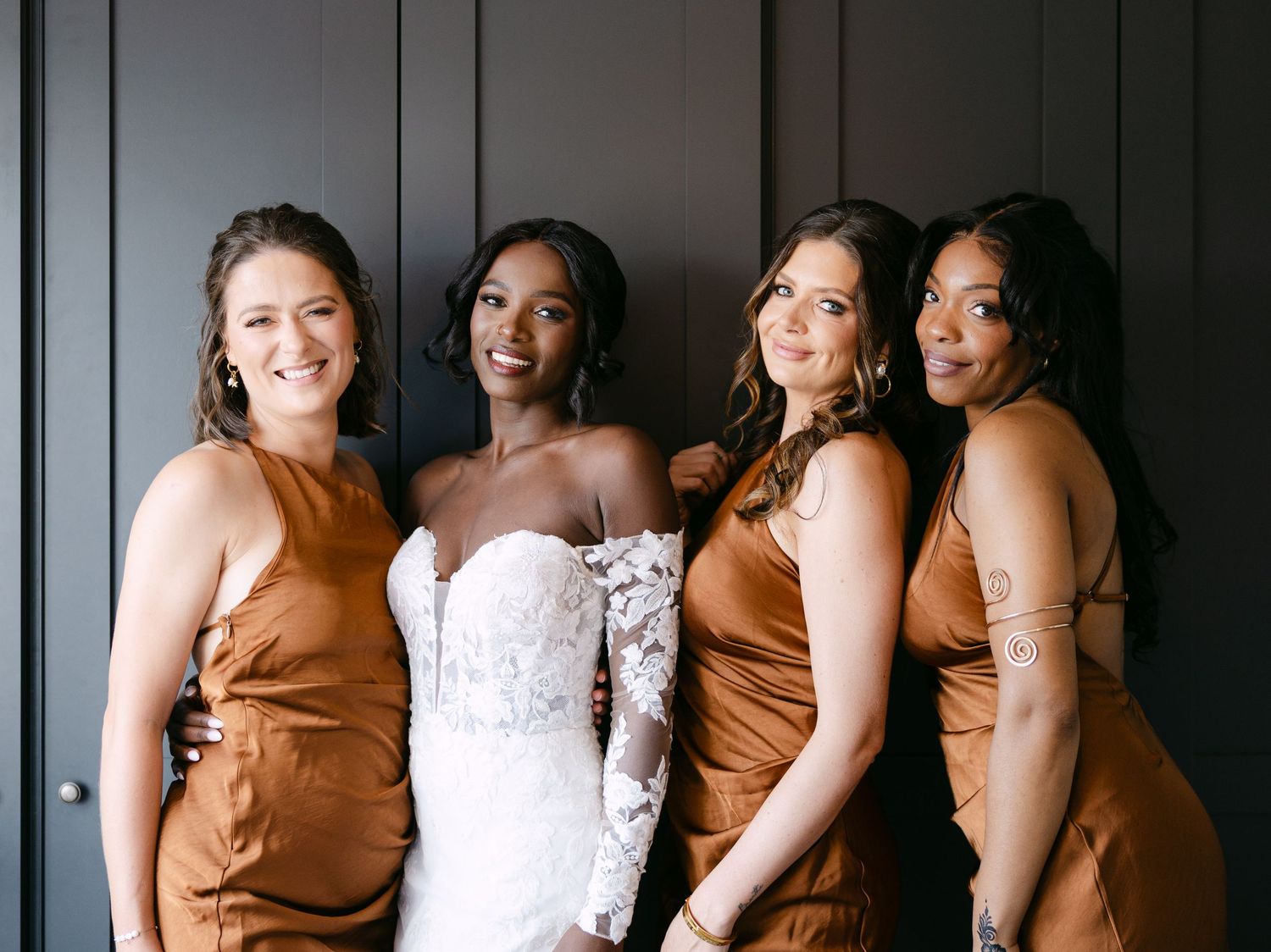 Wedding party group photo with bridesmaids in copper dresses alongside bride in white lace gown.