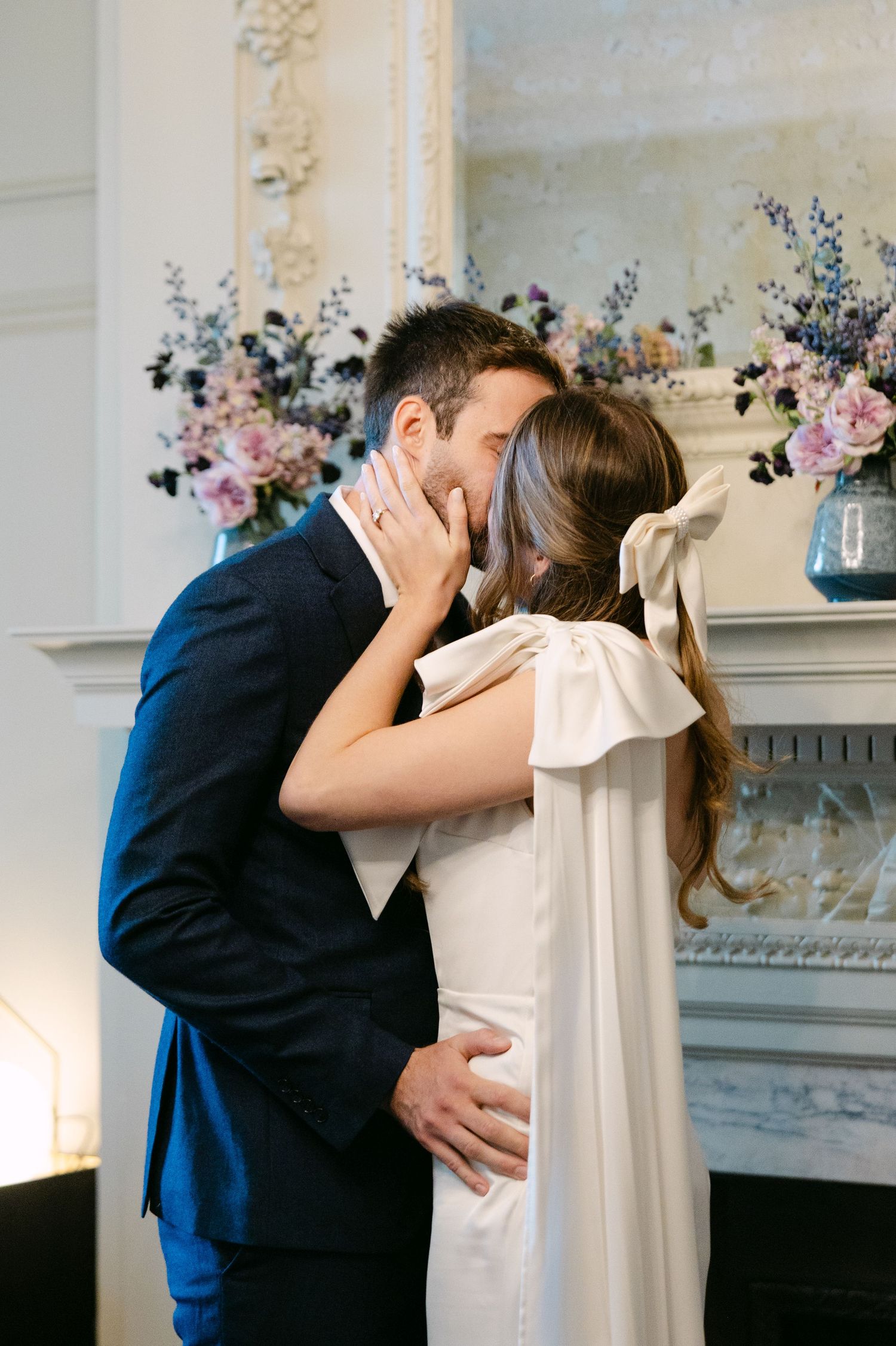 A romantic wedding moment captured indoors with elegant floral arrangements and ornate architectural details.