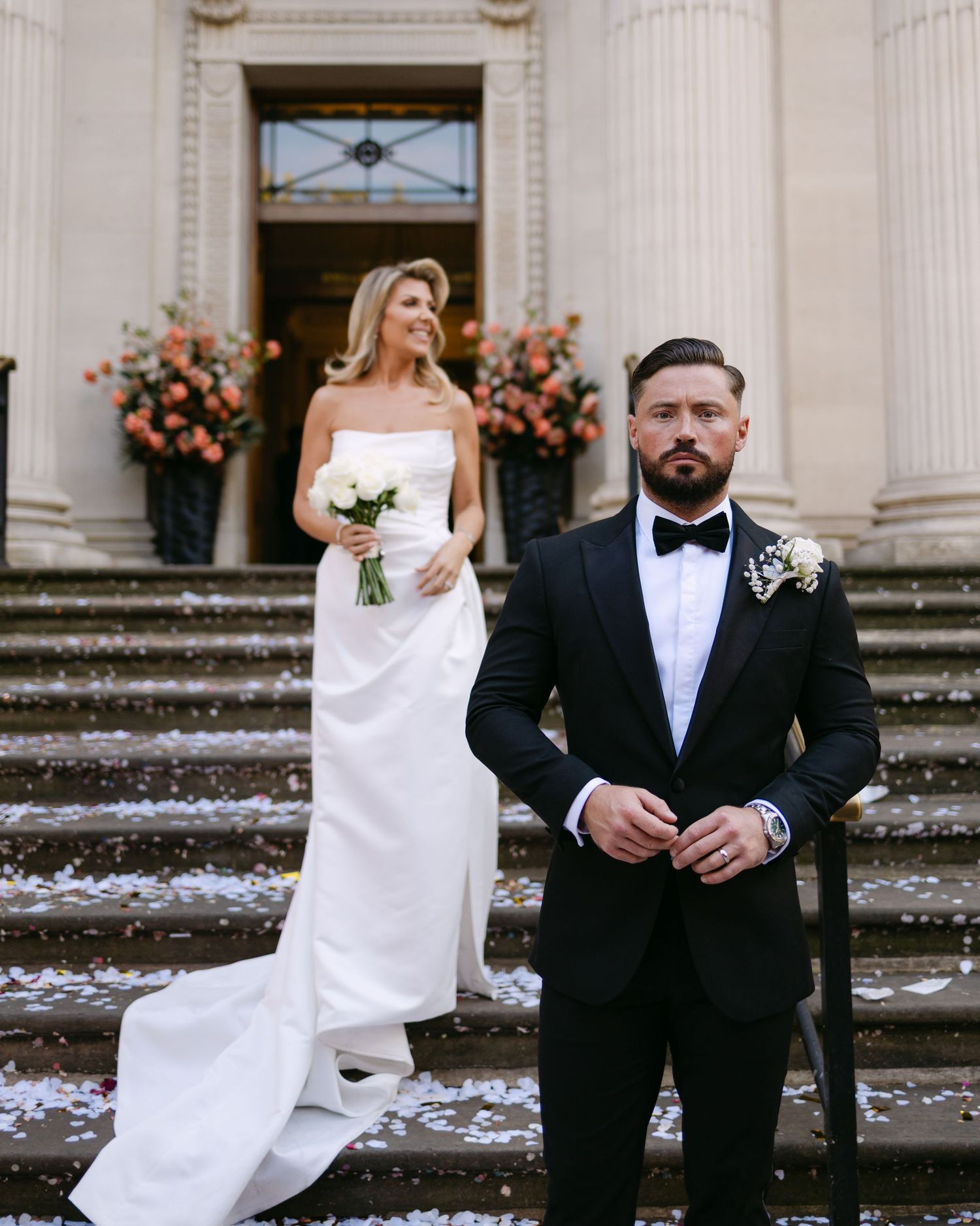 Wedding couple poses on grand stone steps adorned with flower petals.