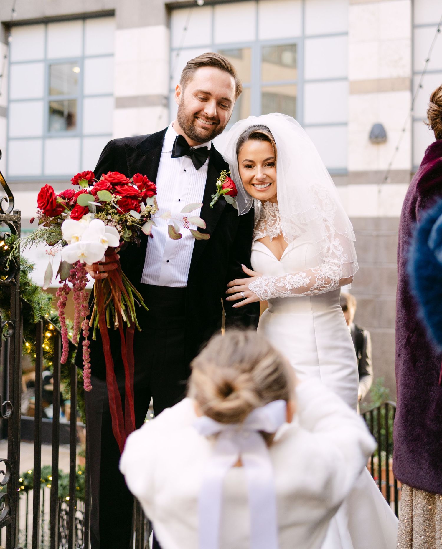 Wedding celebration on outdoor terrace with red floral arrangements.