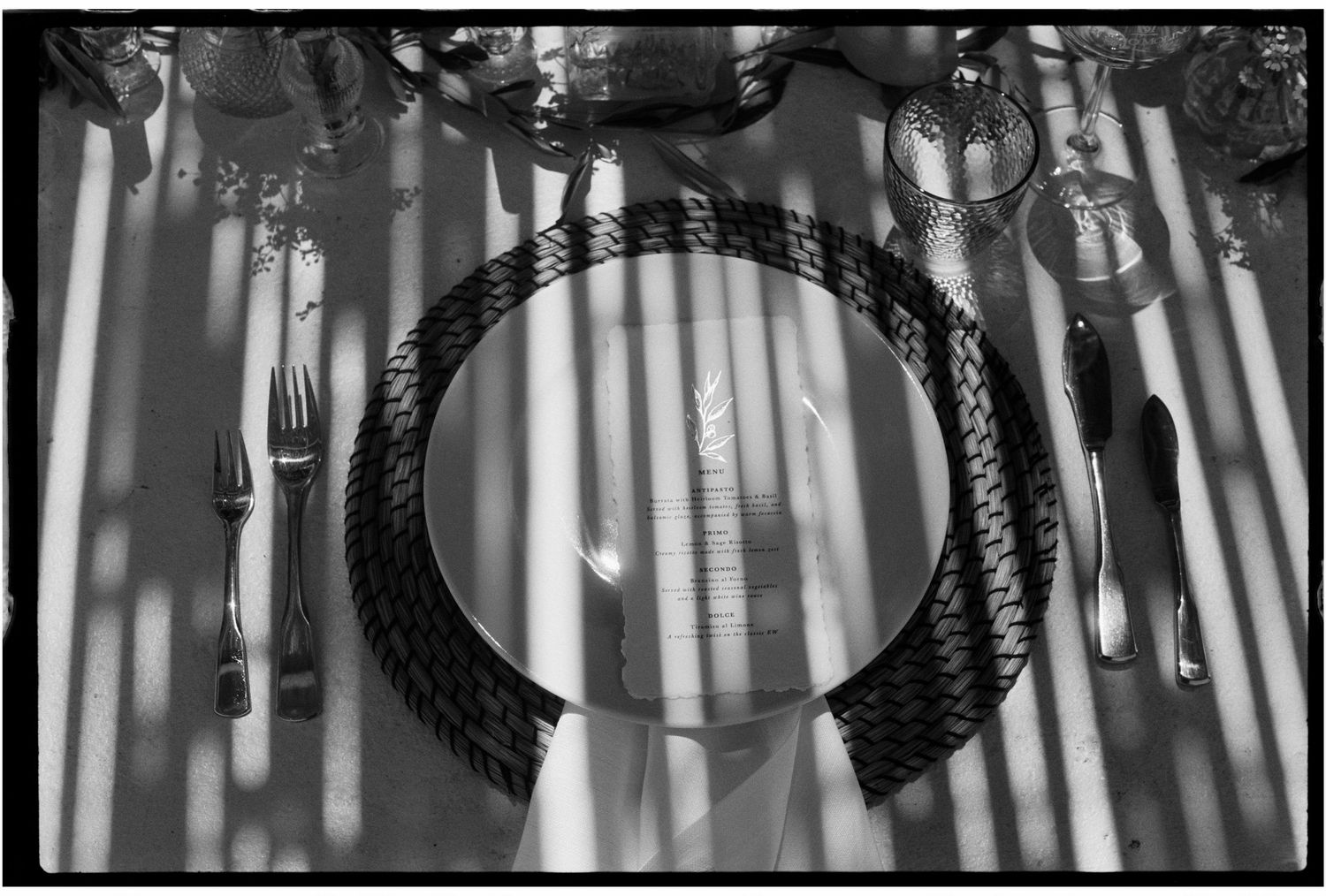 Black and white overhead shot of an elegant place setting with woven charger plate and silverware casting dramatic shadows.