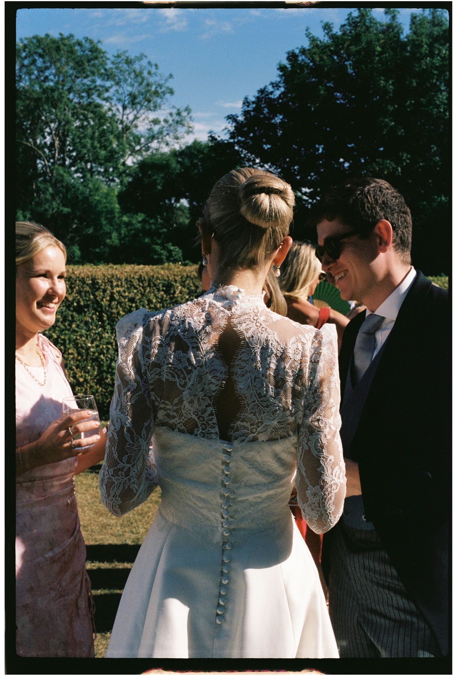 Film photo of a bride in a stunning lace back wedding gown chatting with guests outdoors.