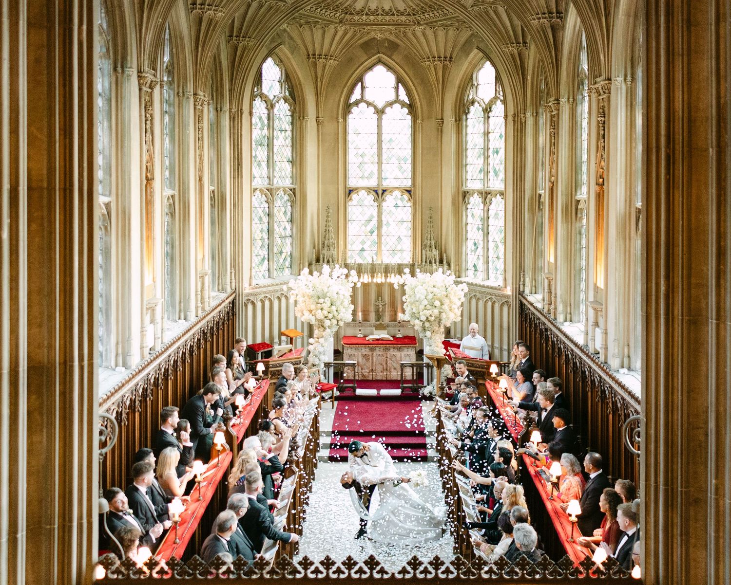 Panoramic view of an elegant church wedding ceremony with ornate Gothic architecture and stained glass windows at Ashridge House.