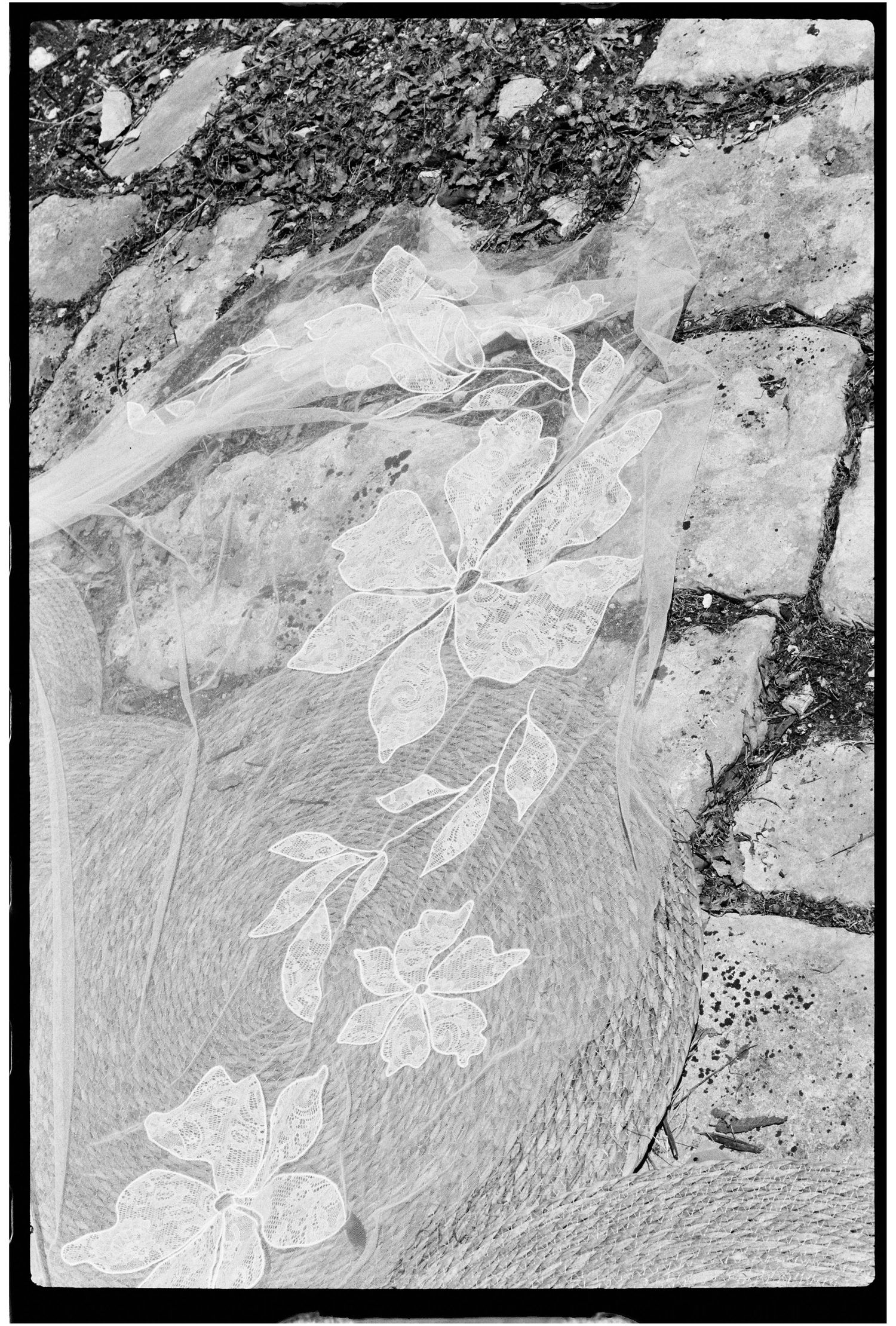 Close-up black and white photo of a delicate floral lace wedding veil laid on stone pavement.
