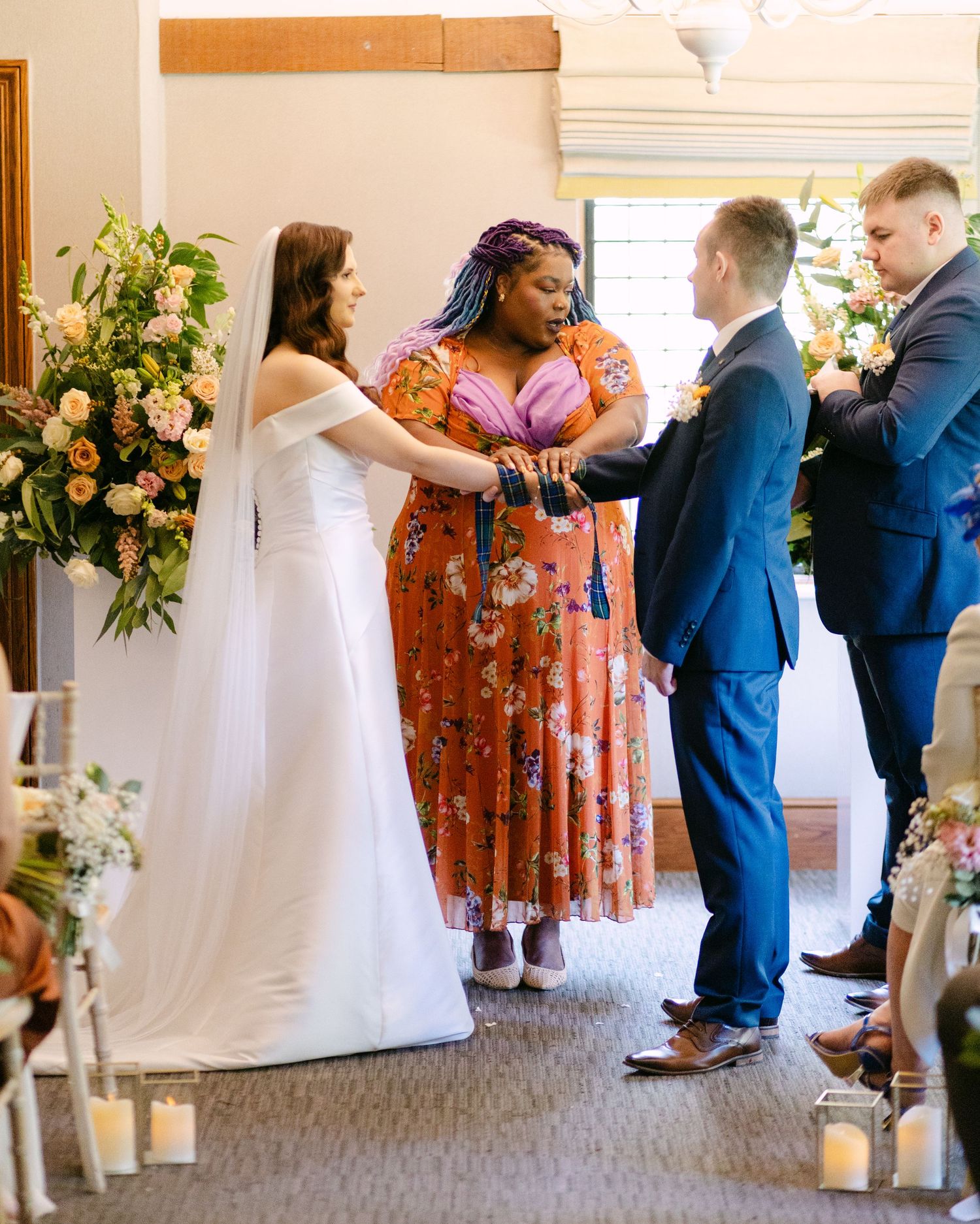 Wedding ceremony processional with attendants in blue suits and floral arrangements.