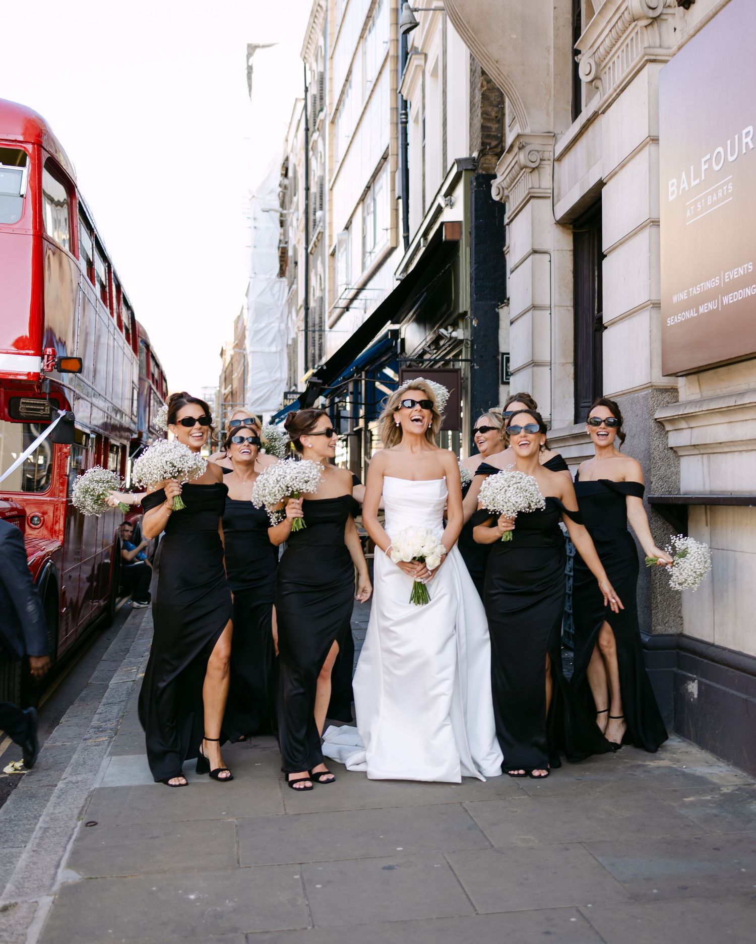 Wedding party members in black attire posing playfully on a city street.