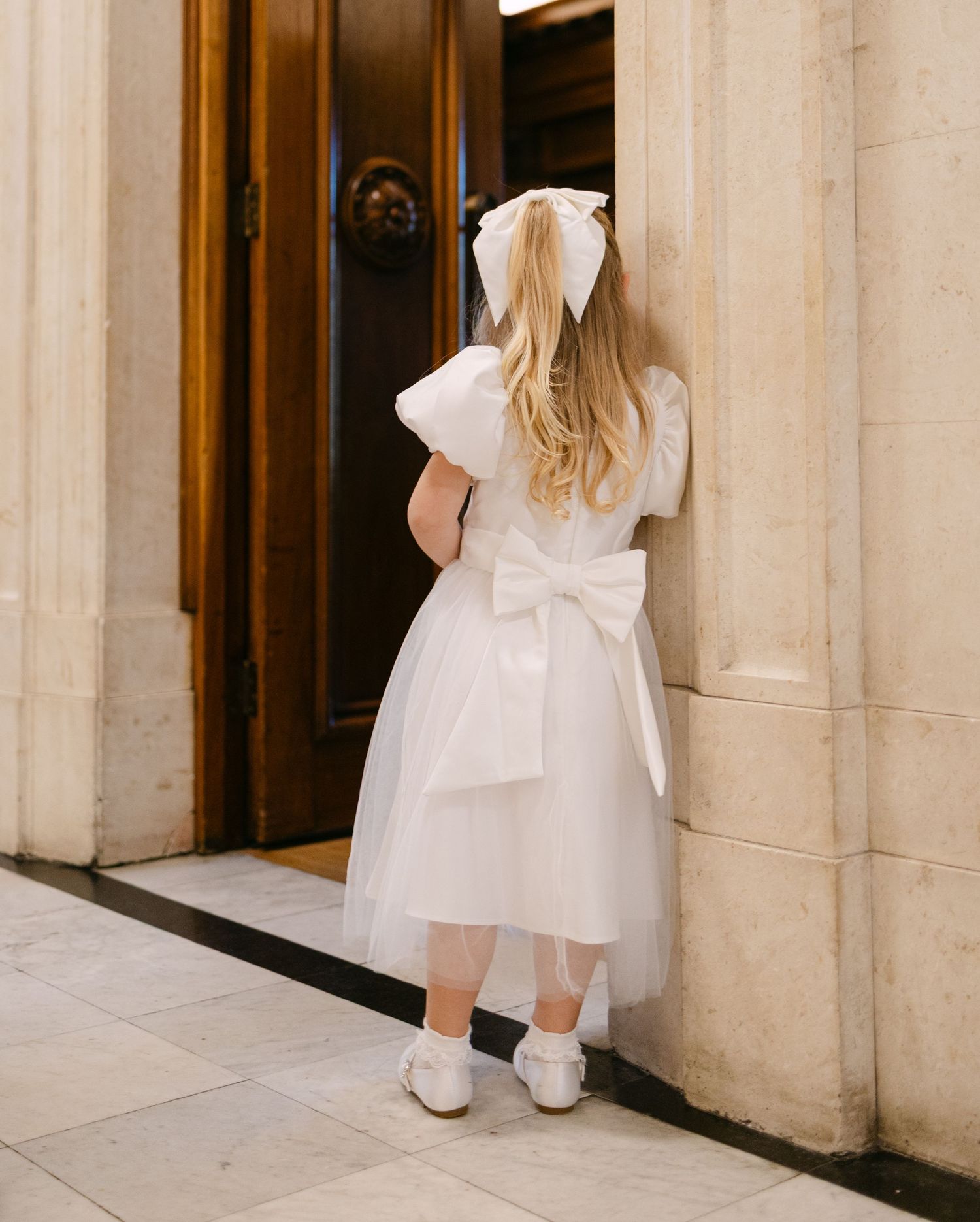 Close-up view of white wedding dress details and shoes against a stone column backdrop.