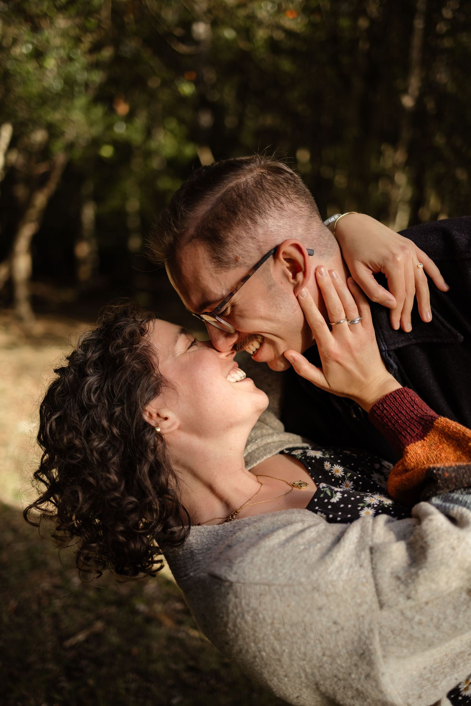 A tender embrace captured in natural outdoor lighting among trees.