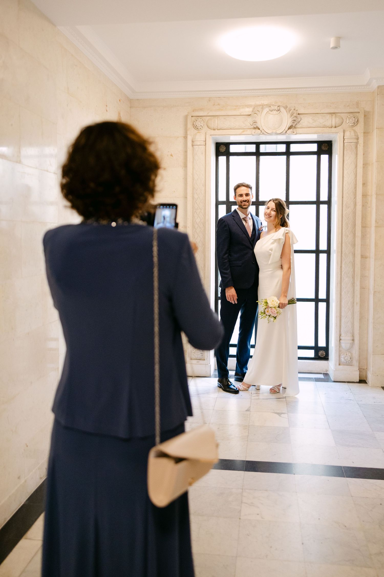 Mum captures a couple's first look moment in an elegant white hallway at The Old Marylebone Town Hall.