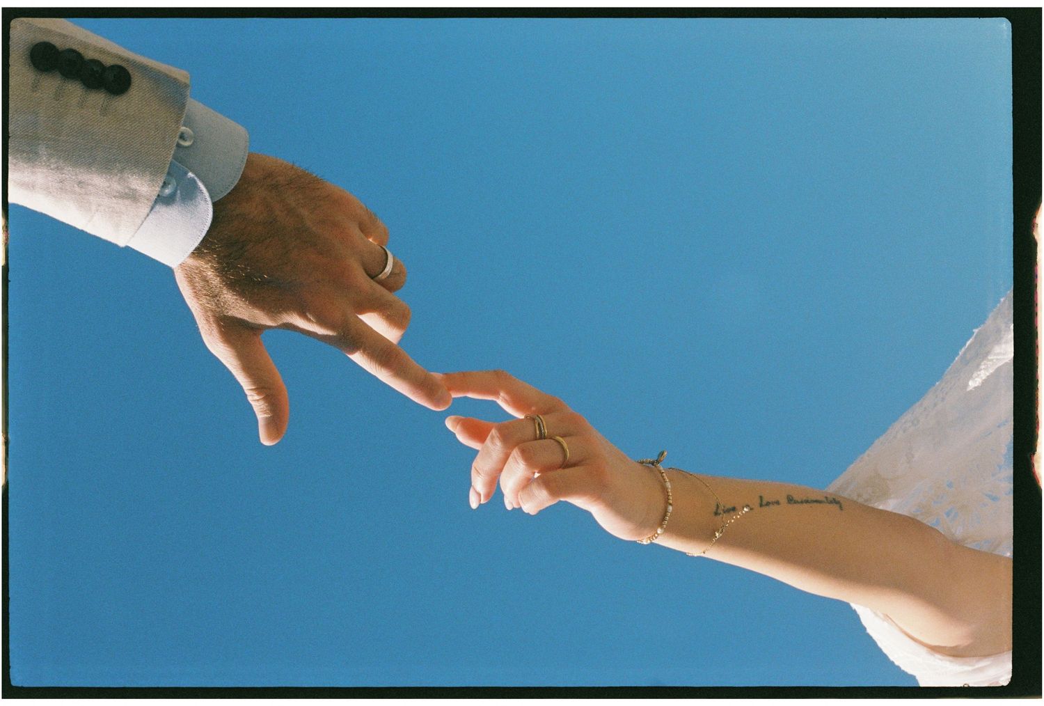 Bride and groom touching fingertips against a clear blue sky in a romantic gesture.