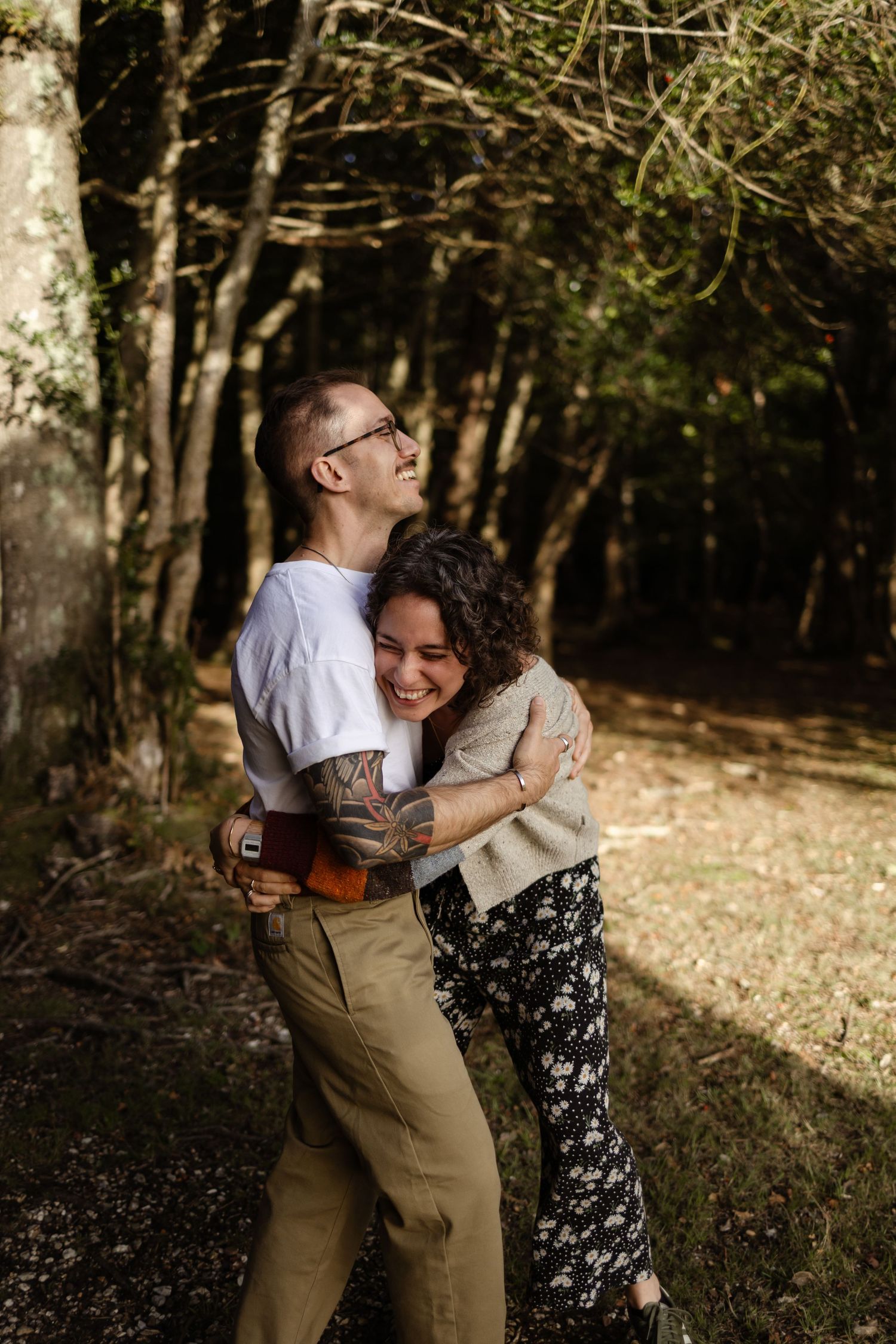 A couple embracing and laughing together in a sunlit forest setting.