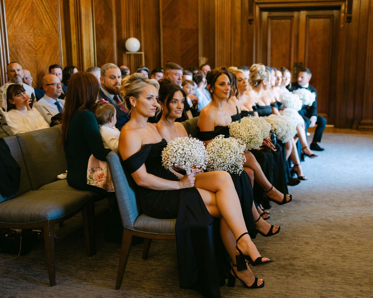 Wedding reception guests seated in elegant wooden chairs during indoor ceremony.