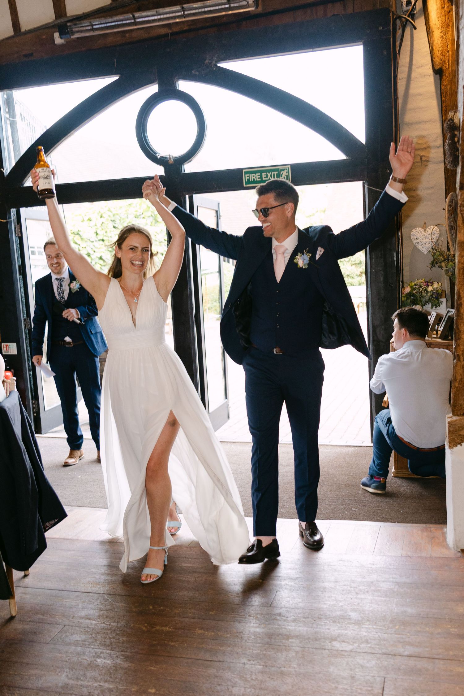 Bride and groom make joyful grand entrance at rustic barn wedding venue, raising hands in celebration.