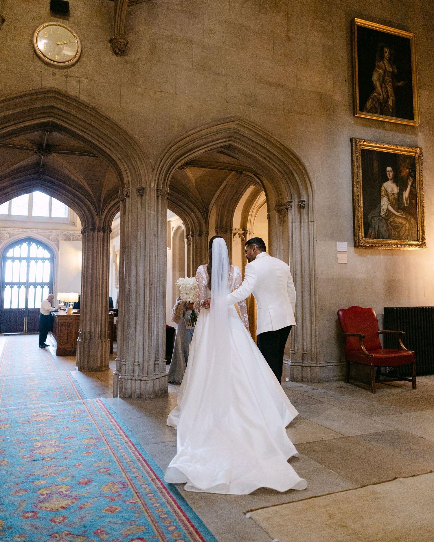 Wedding dress displayed in a stone hallway with arched windows and decorative carpet at Ashridge House, Hertfordshire.