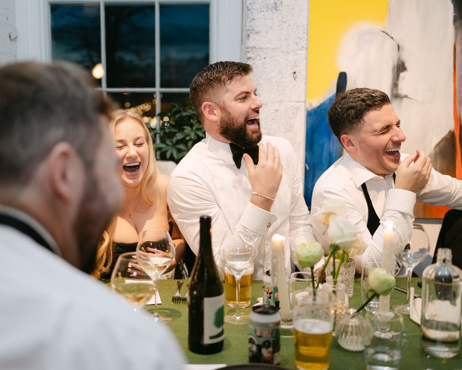 Wedding guests laughing and socializing at reception with colorful drinks.