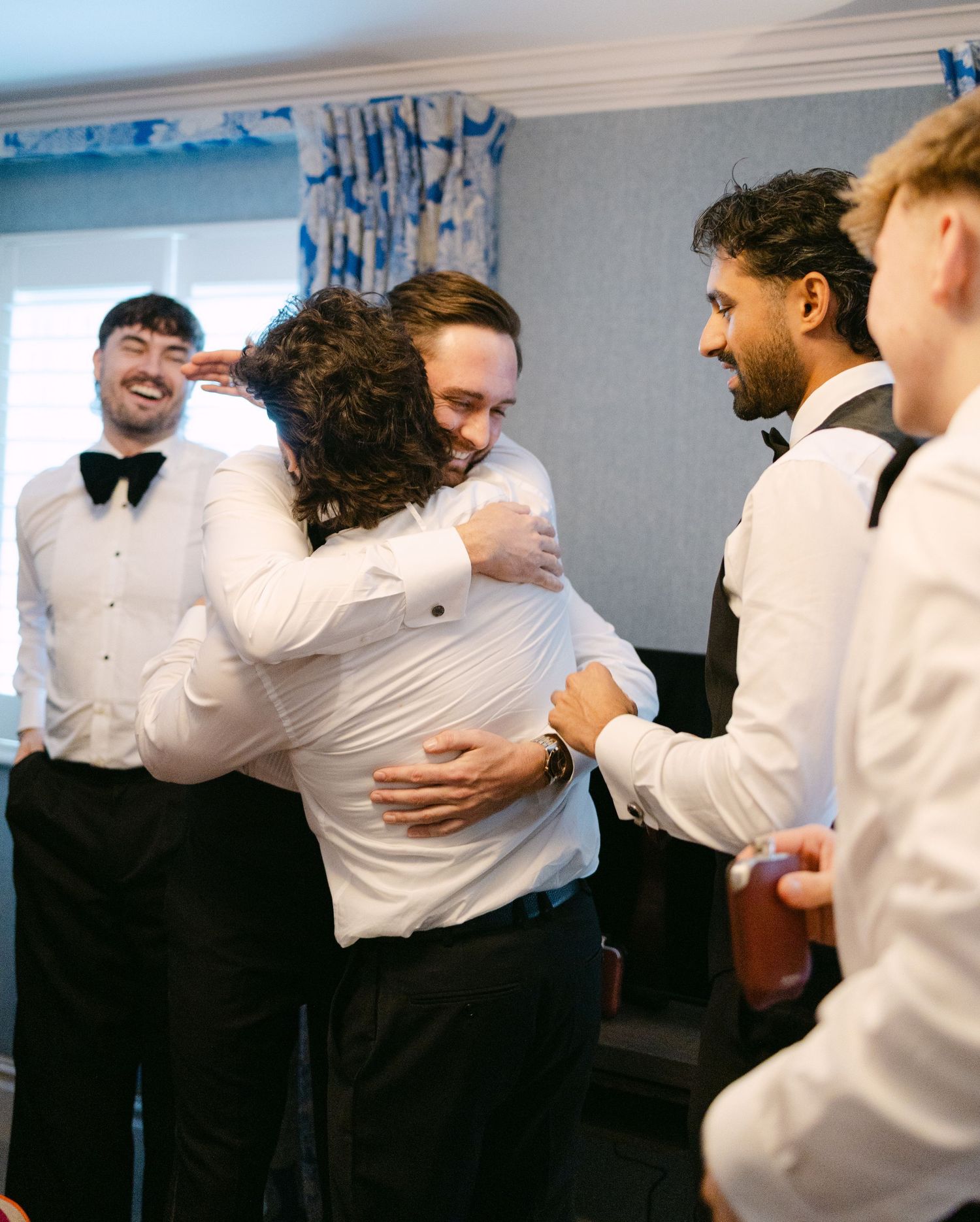 Wedding party members in formal attire share emotional hugs and embraces.