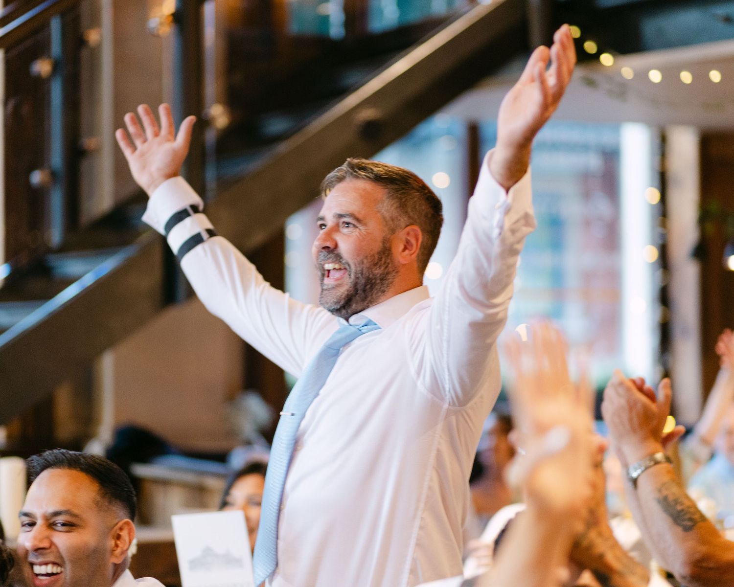 A guest celebrates with raised arms during an energetic wedding reception moment.