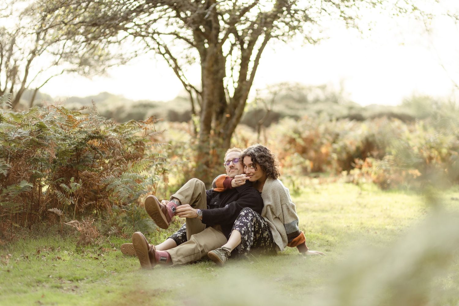 Romantic couple's photoshoot in a sunlit meadow with trees in background.