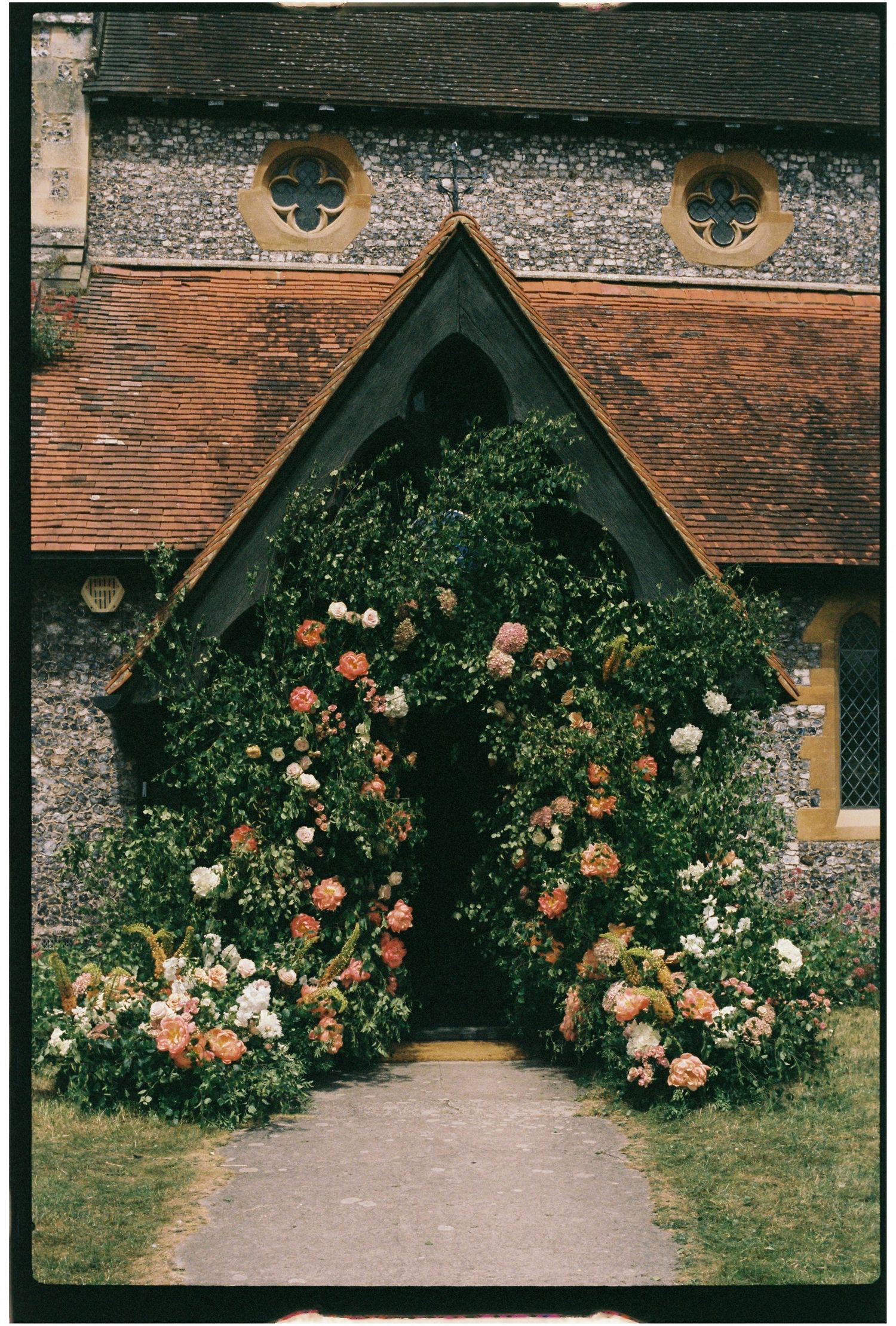 Stunning church entrance adorned with lush floral arch of pink and peach blooms for a wedding.