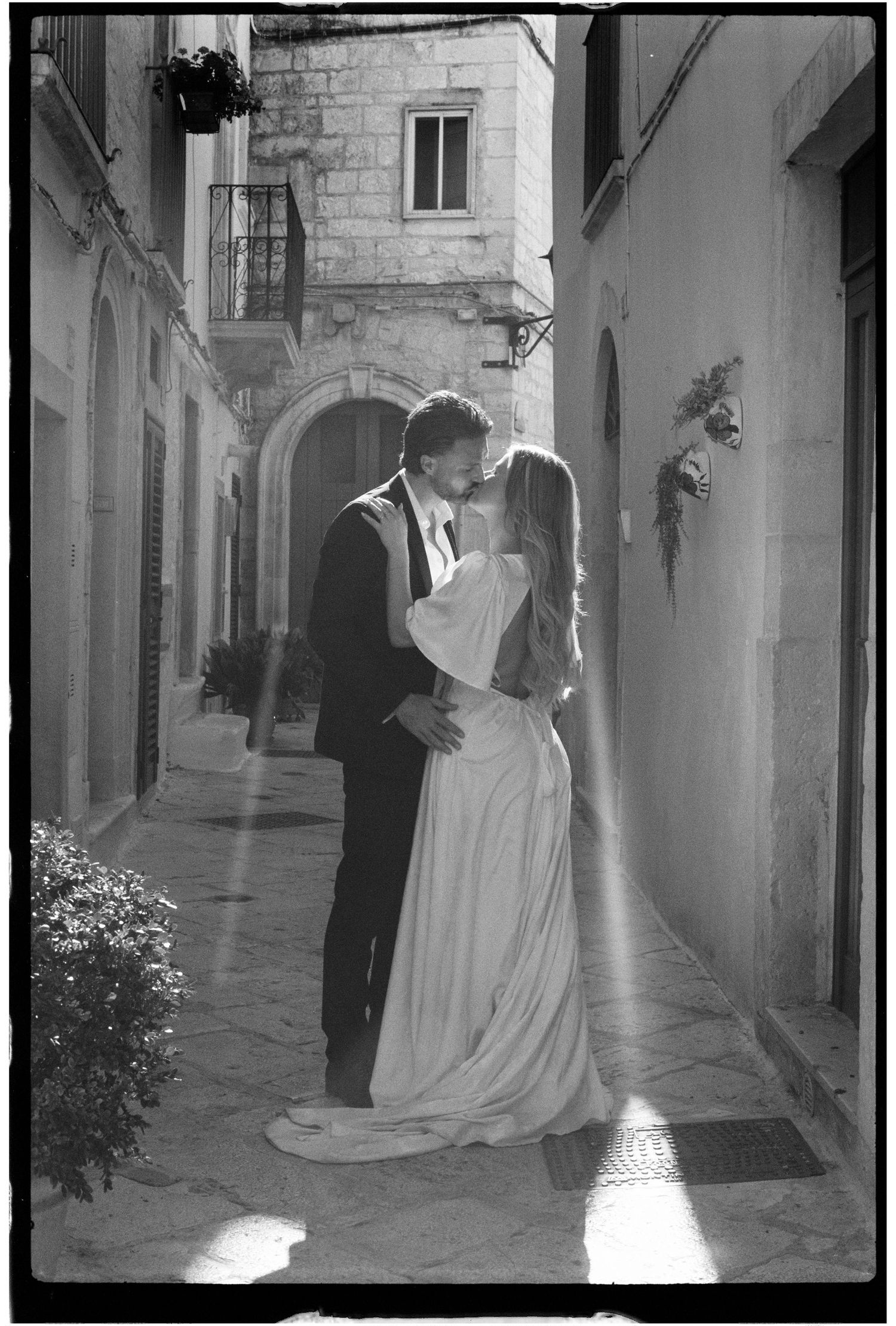 Black and white photo of a bride and groom sharing a kiss in a charming European cobblestone alleyway.