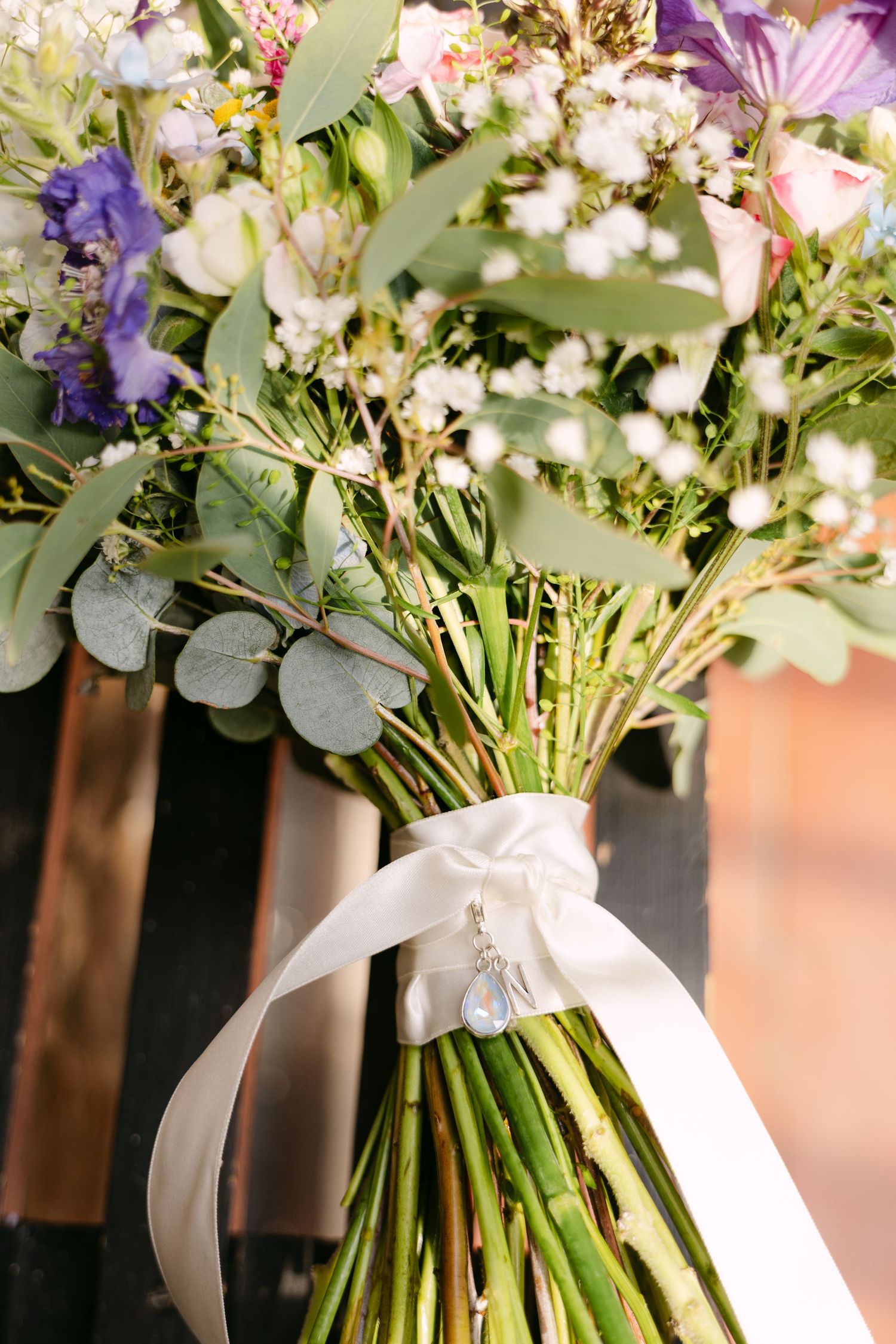 Bridal bouquet with purple, pink, and white wildflowers tied with a white satin ribbon and charm.