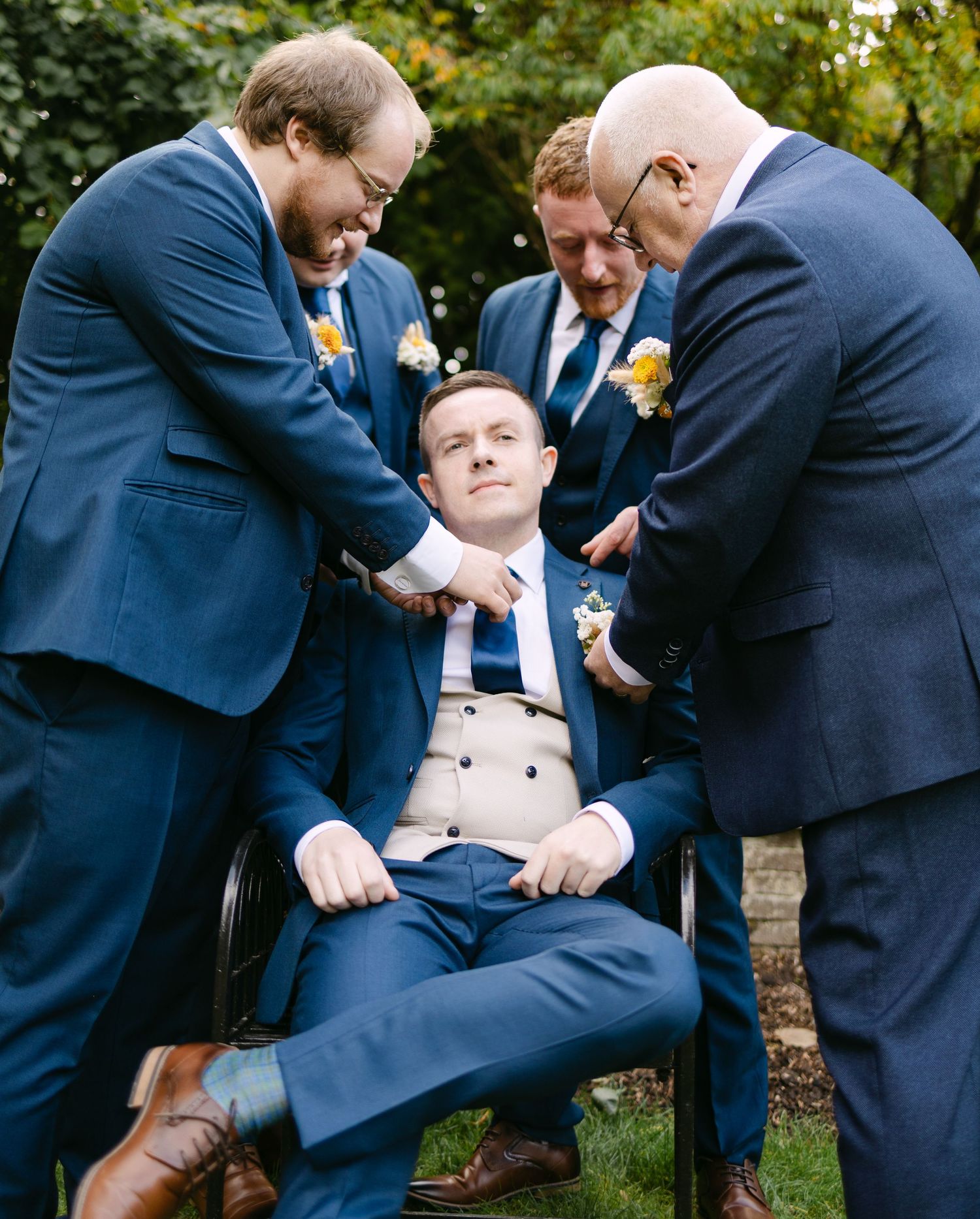 Groomsmen playfully adjusting each other's ties and suits outdoors.