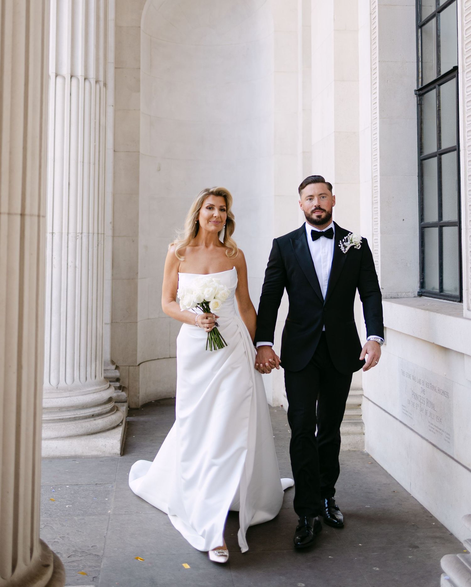 Couple walks through classical columned hallway in wedding attire.