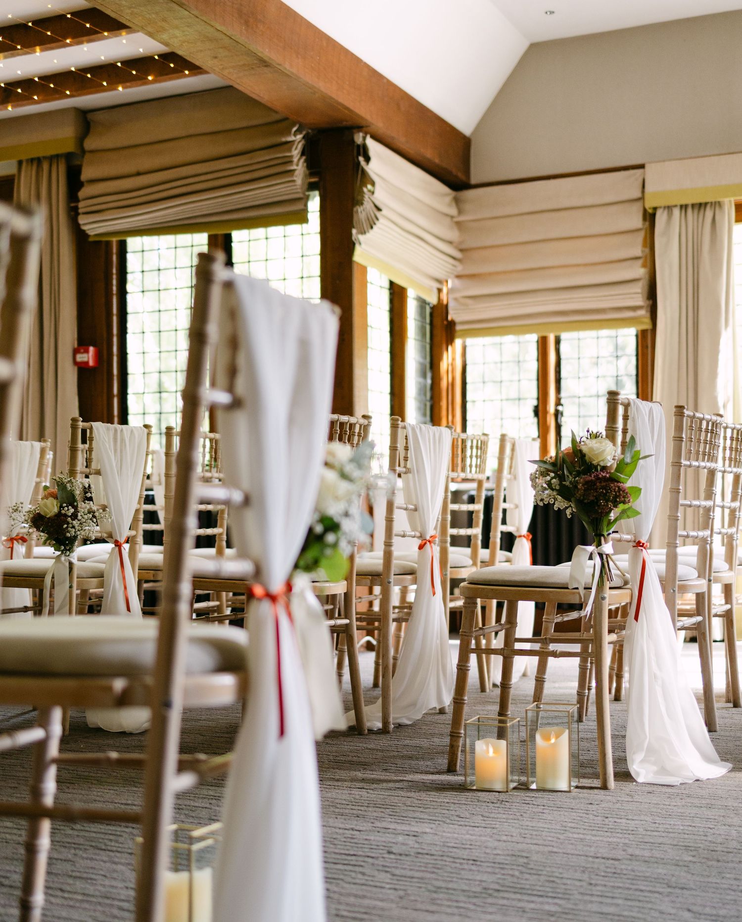 Wedding ceremony setup with white chairs and decorative fabric drapes in an indoor venue.