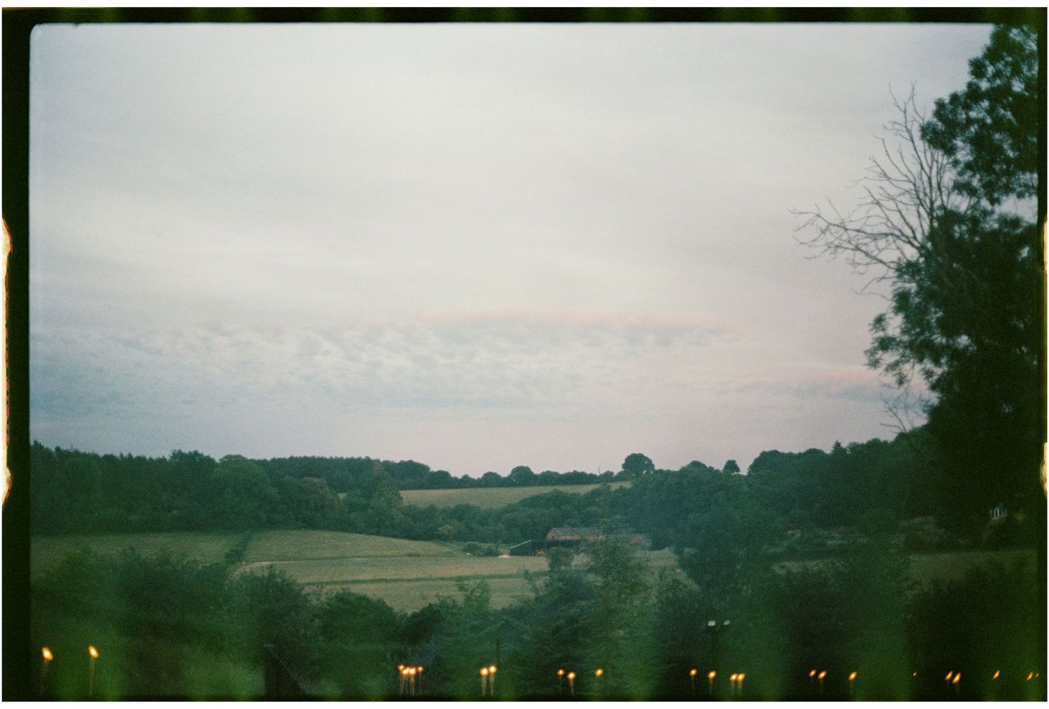 Serene countryside landscape at dusk with rolling green fields and soft glowing lights below.