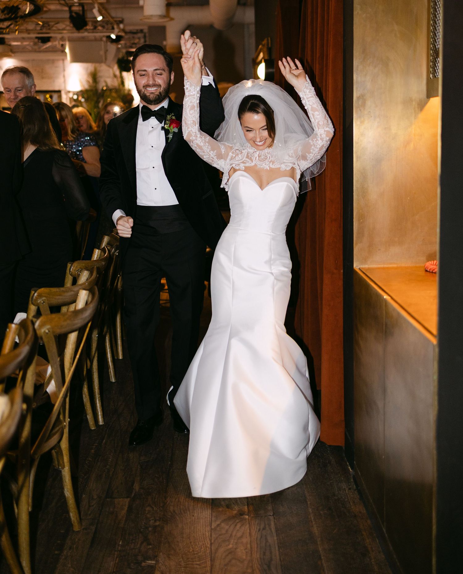 Wedding couple and guests dance joyfully on a wooden floor during the reception celebration.