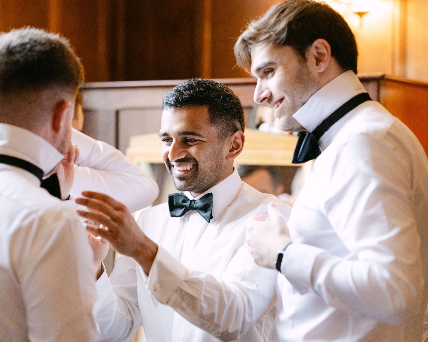 Groomsmen in white shirts and bowties sharing laughs while getting ready.