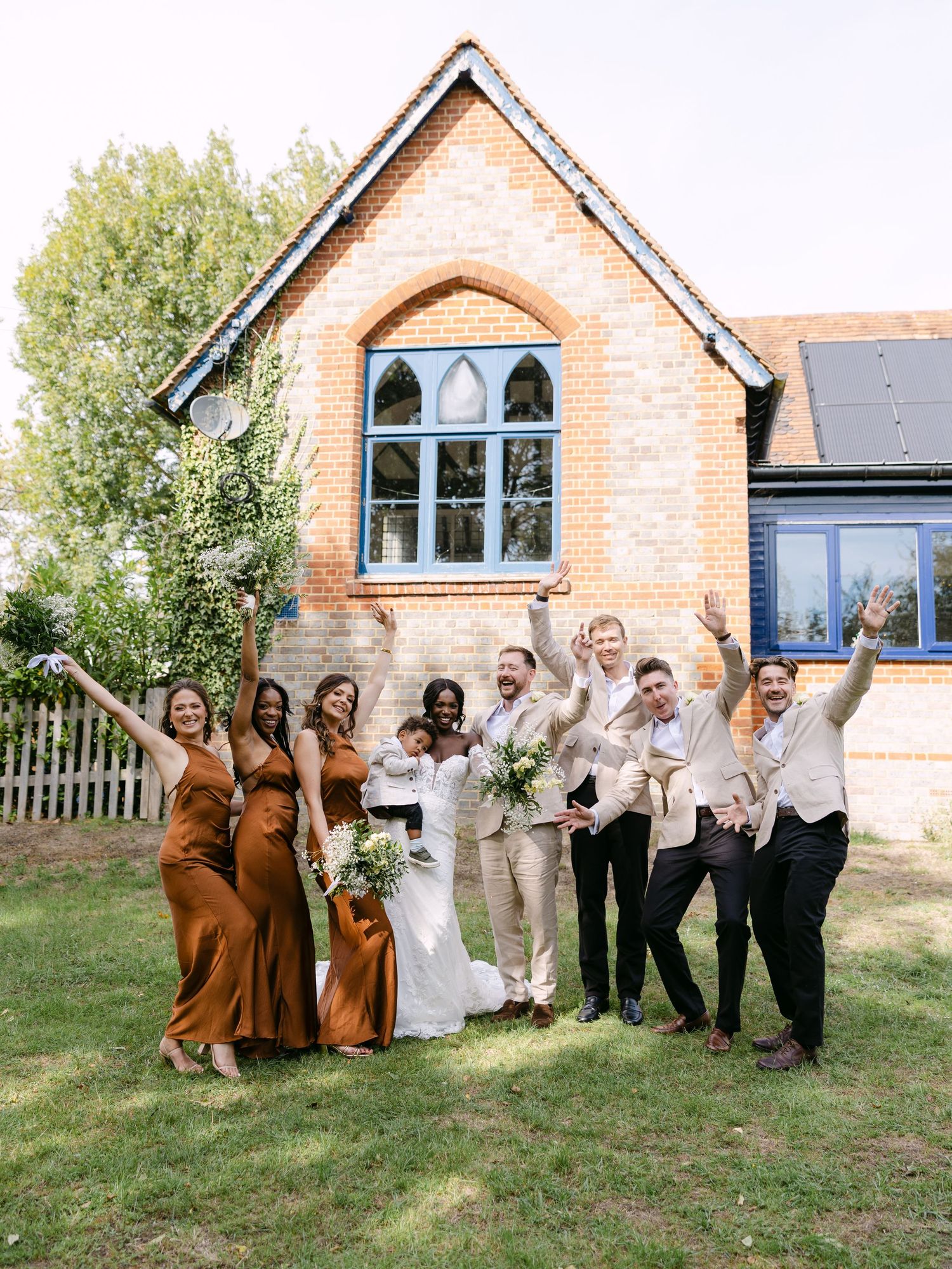 Wedding party posing playfully in front of a rustic brick church building.