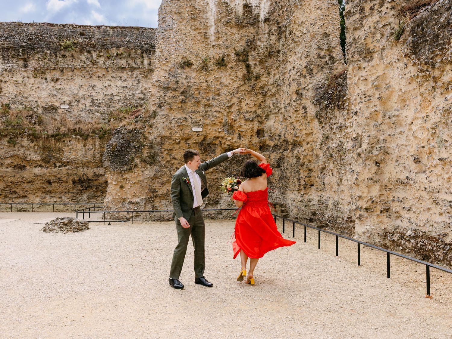 Couple dancing in red dress and green suit near ancient stone castle ruins on a windy day.