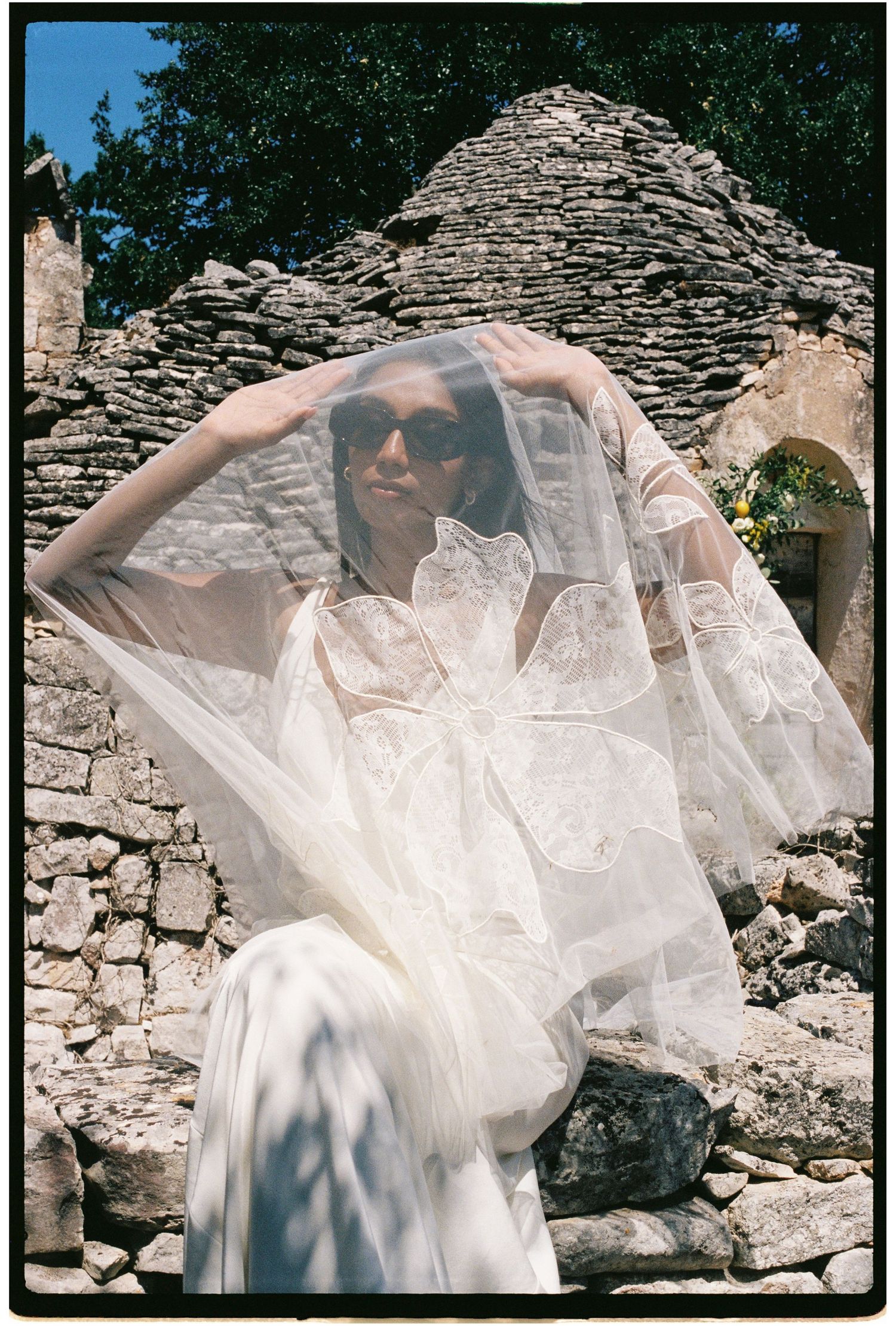 Bride in white gown and veil posing among ancient stone ruins on a sunny day.