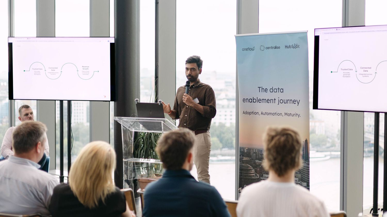 Professional presenting data enablement journey at a modern business conference with audience and branded banner.