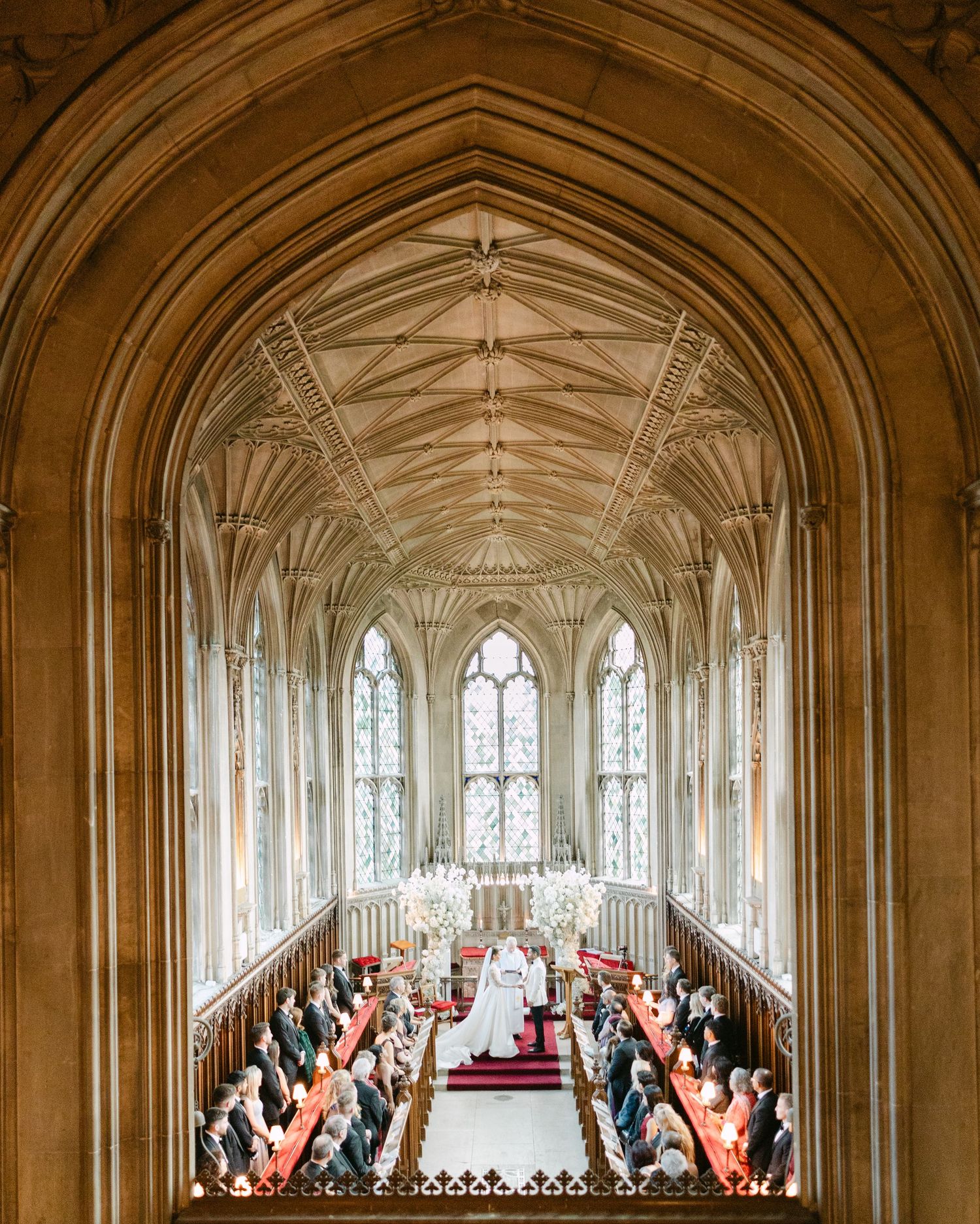 Panoramic view of a cathedral wedding ceremony with guests seated along wooden pews at Ashridge House, Hertfordshire.