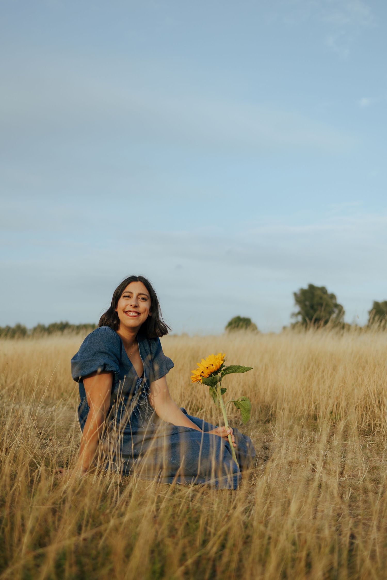 A couple lies in a golden field of tall grass on a sunny afternoon.