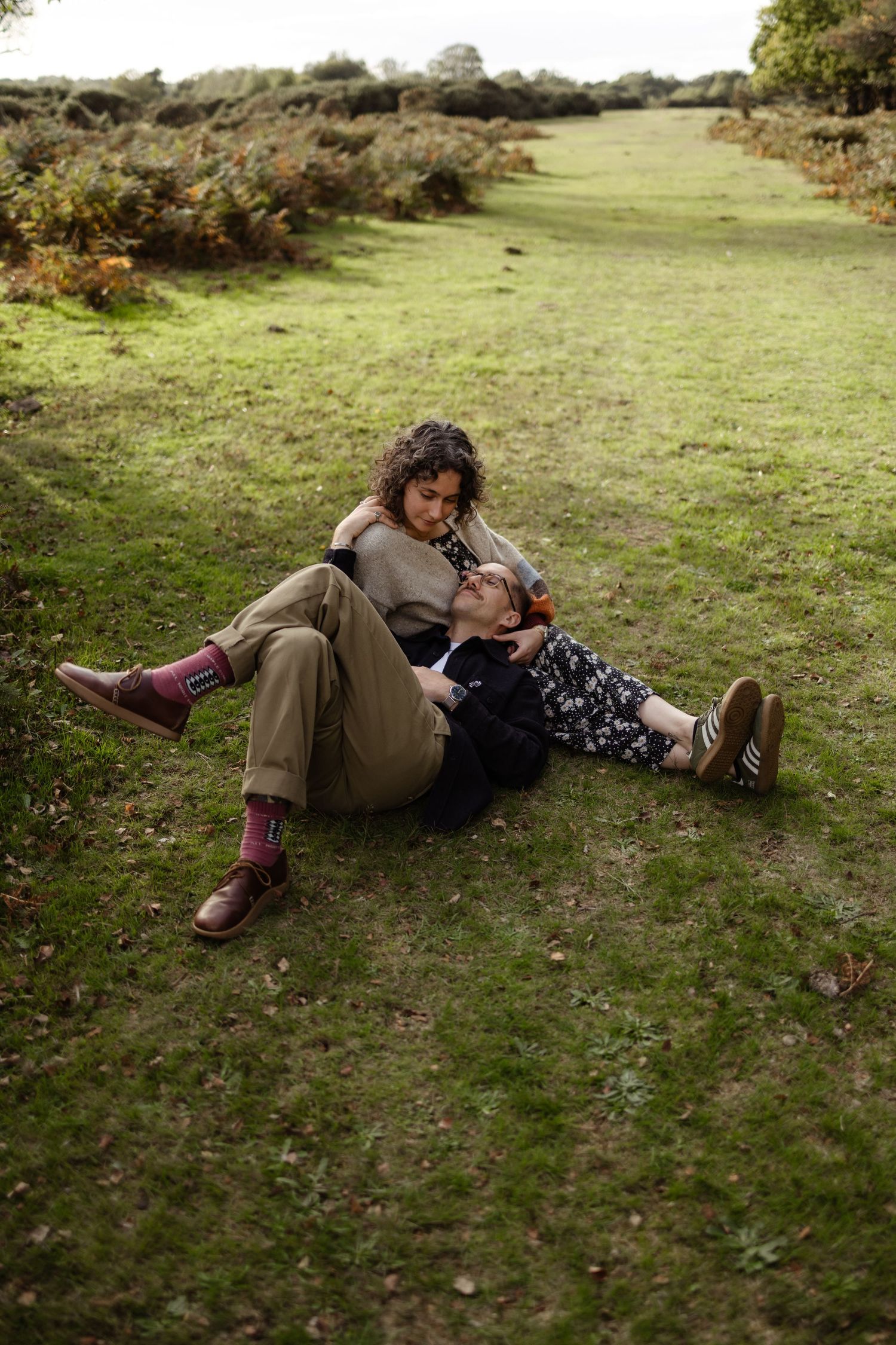 Two people relaxing on grass during an outdoor autumn photoshoot.