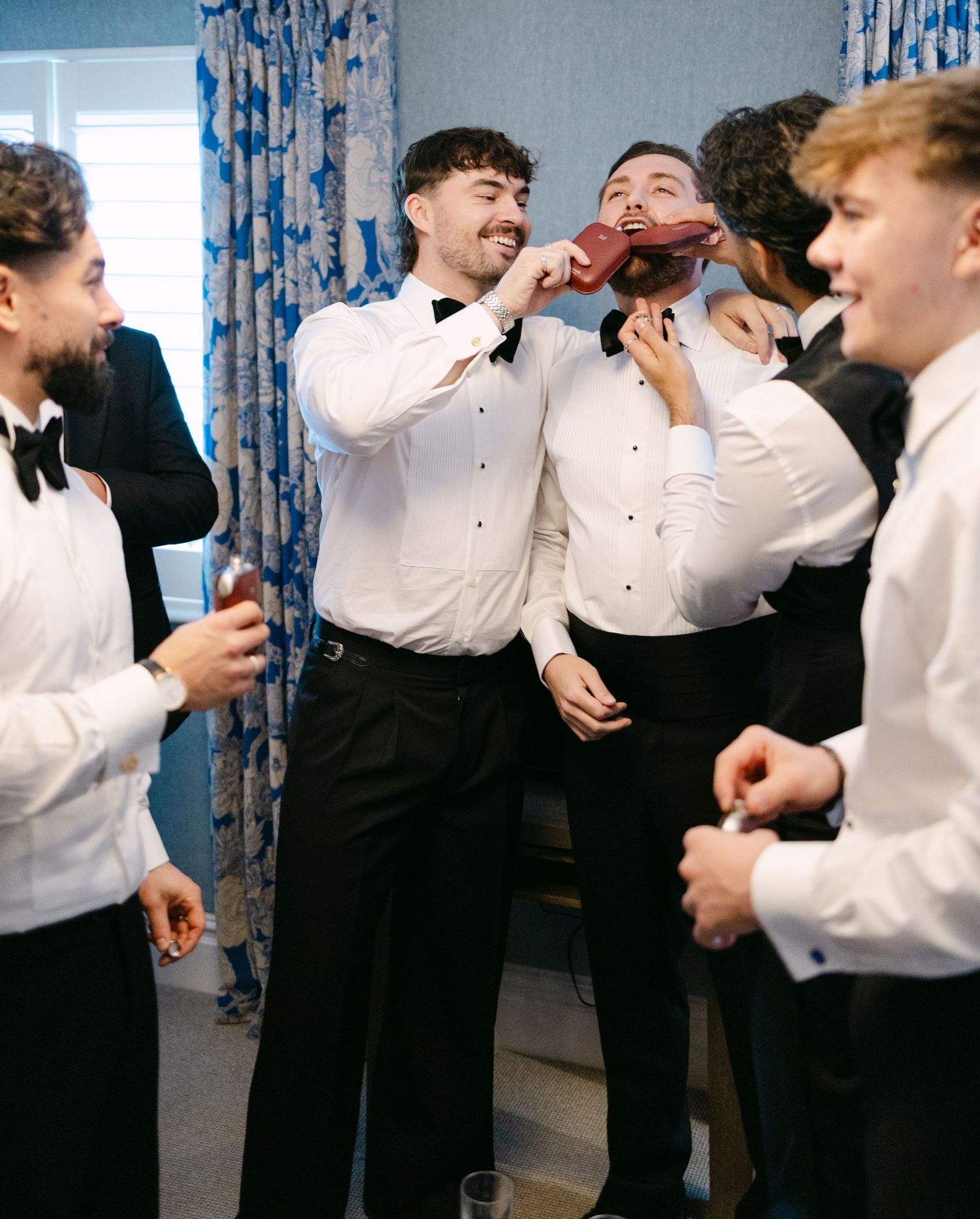 Groomsmen in white shirts and bowties share laughs during pre-wedding preparations.