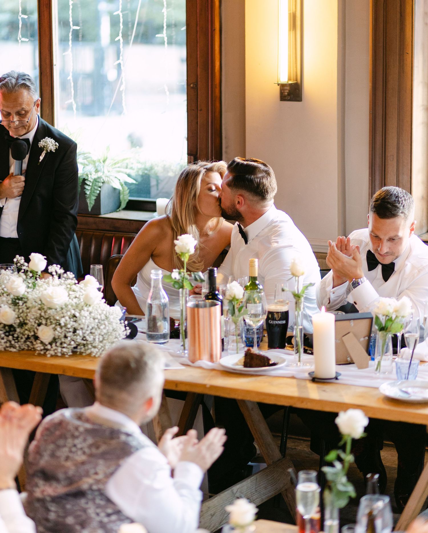 A romantic moment unfolds during wedding speeches at an elegant indoor venue.