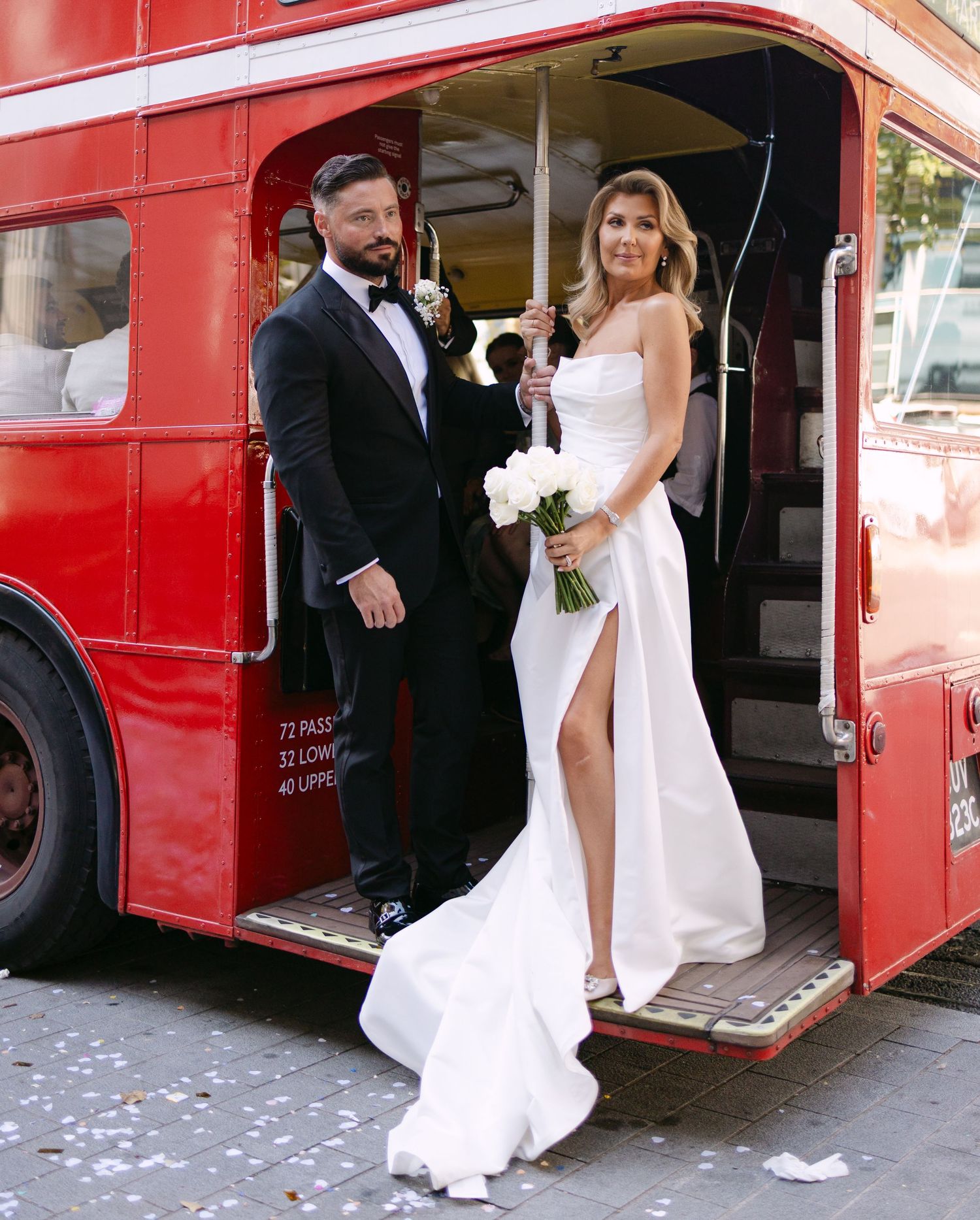 Wedding couple poses beside classic red London double-decker bus.
