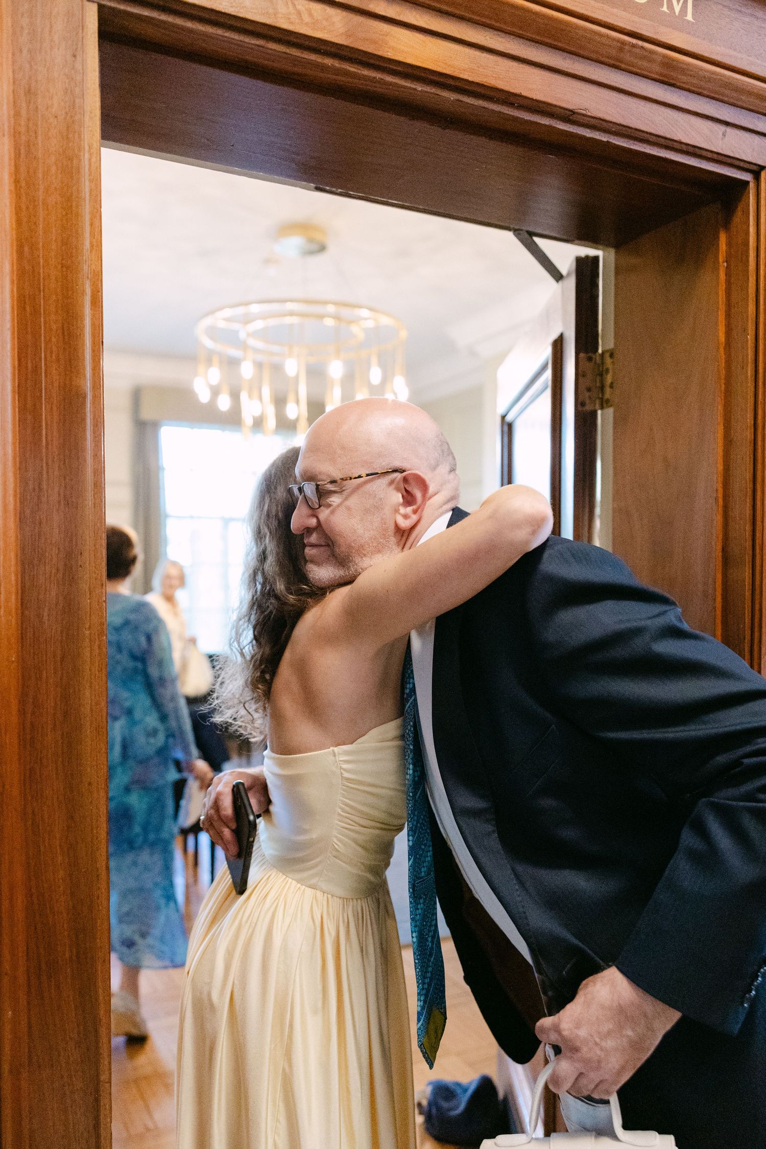 A couple shares a candid moment in a wood-paneled hallway with a yellow dress and dark suit.