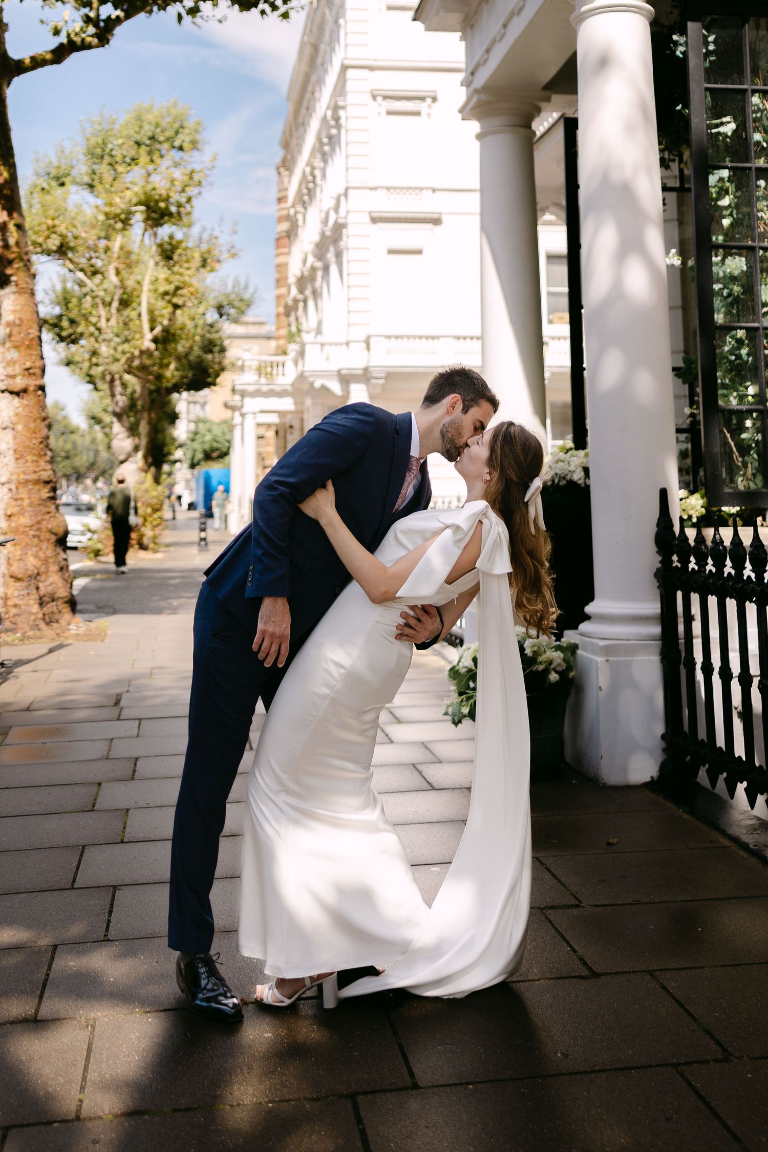 A romantic wedding couple shares intimate moments on a columned porch with white pillars and stone flooring in Kensington, London.