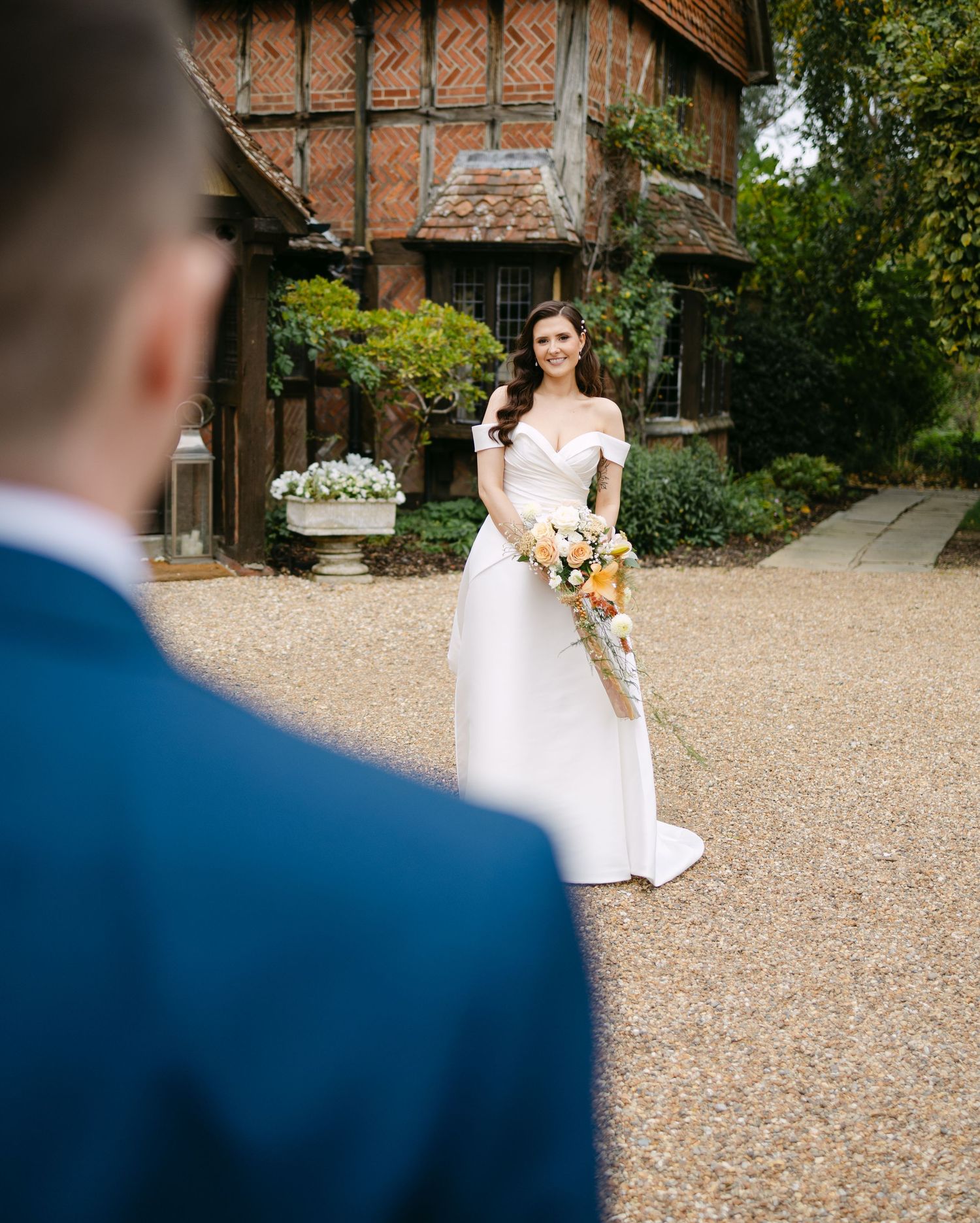 Wedding couple poses on gravel driveway of Tudor-style venue.
