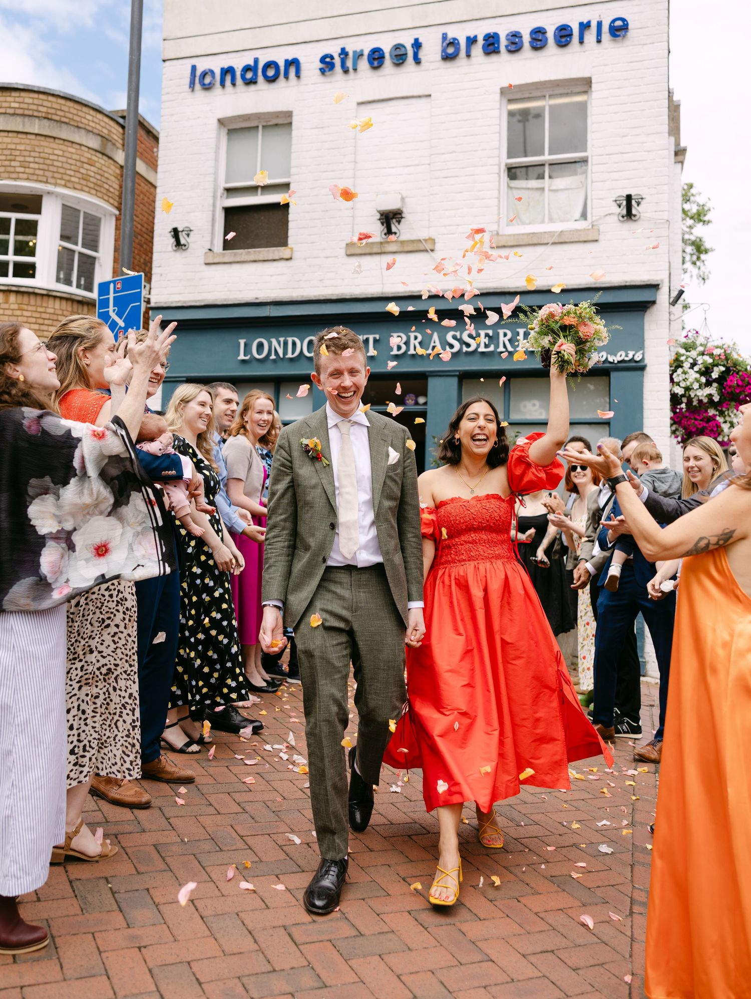 Wedding party exits London Street Brasserie while guests throw confetti in celebration.